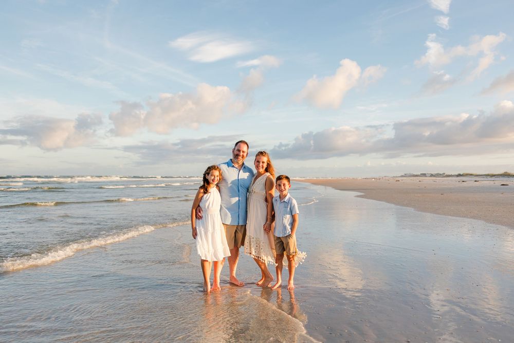 Family portrait session on a beach with gentle waves and cloudy sunset sky.