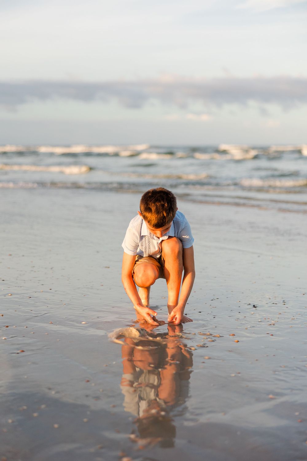 Person crouching to examine reflections in wet sand at the beach.