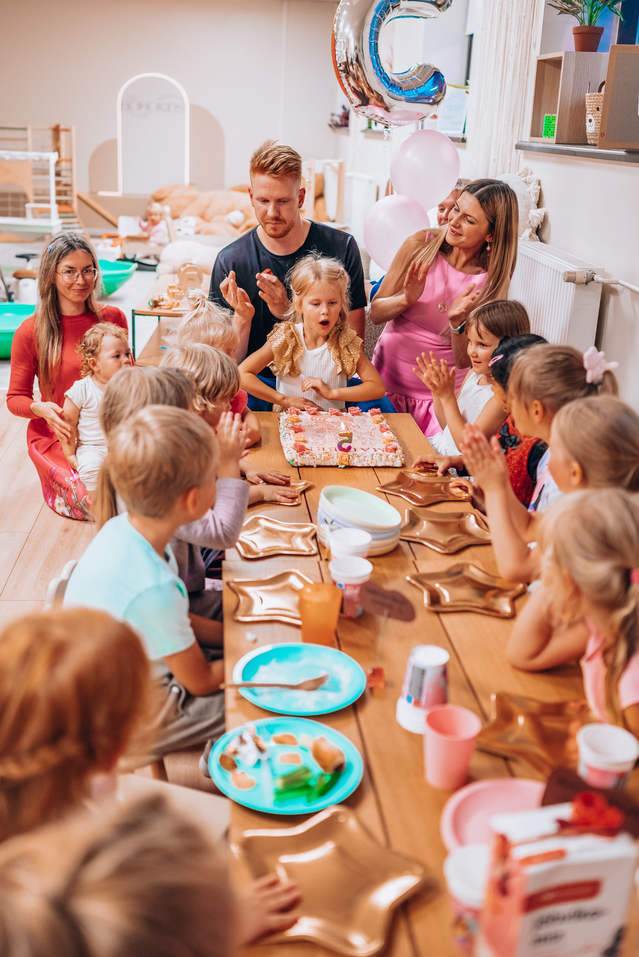 Children participate in a creative workshop activity at a long table in a bright classroom setting.