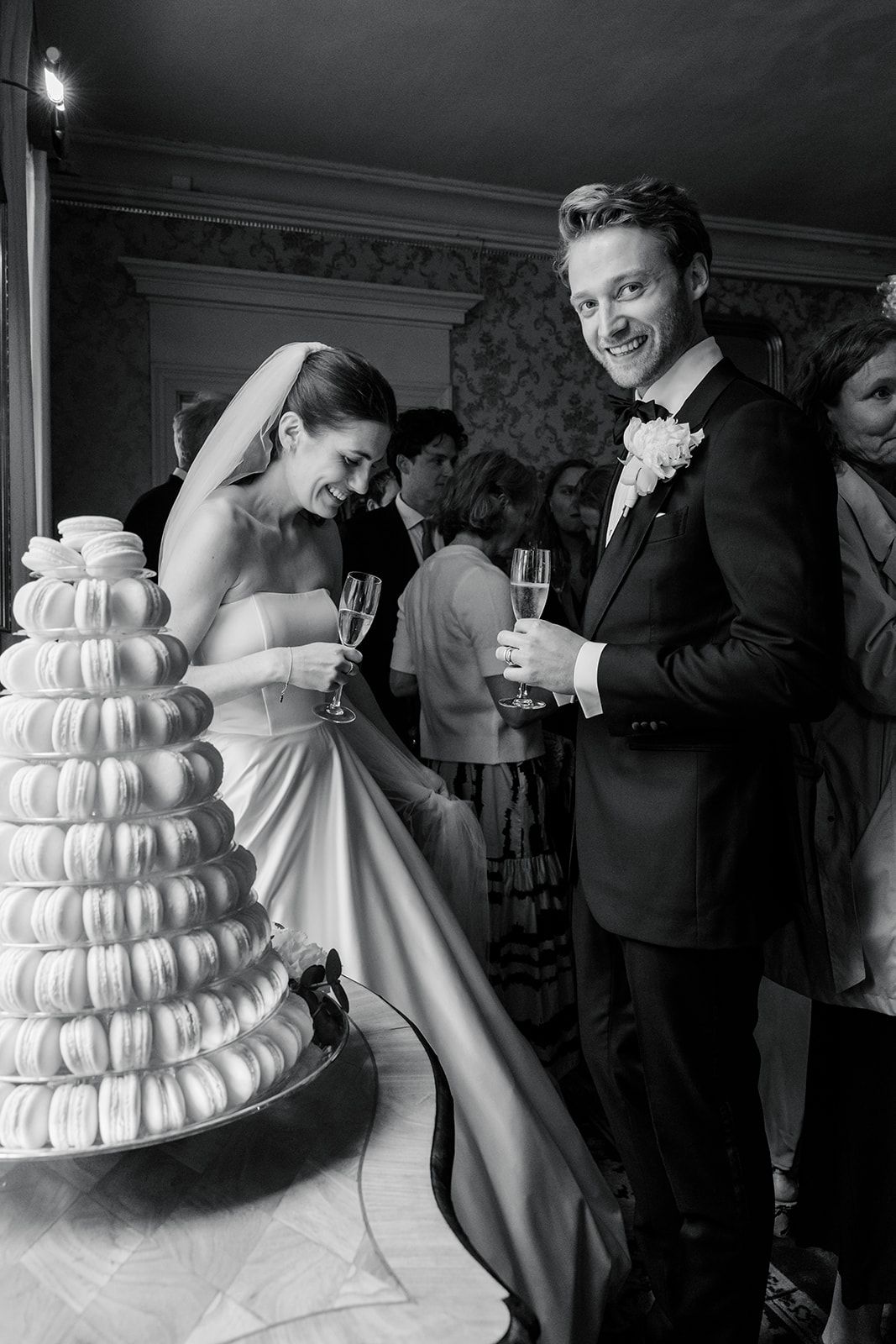 A black and white wedding photo series showing a couple dancing with a tiered meringue cake in the background.