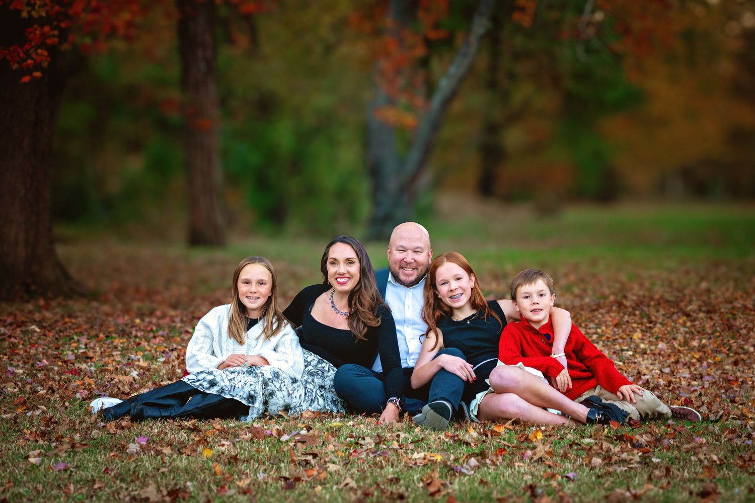 A group lies together on autumn leaves during an outdoor photo session in a wooded area.