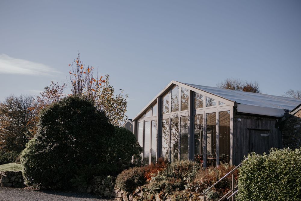 Modern barn wedding venue with large glass windows and manicured gardens under a clear blue sky.