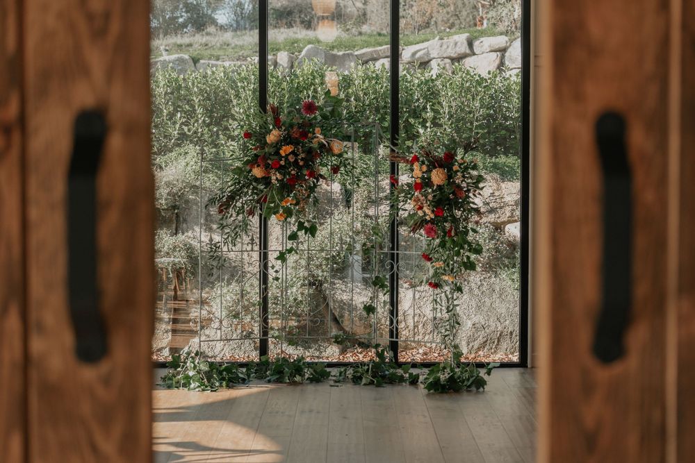 Elegant floral arch display framed by wooden doors with lush greenery and colorful blooms.