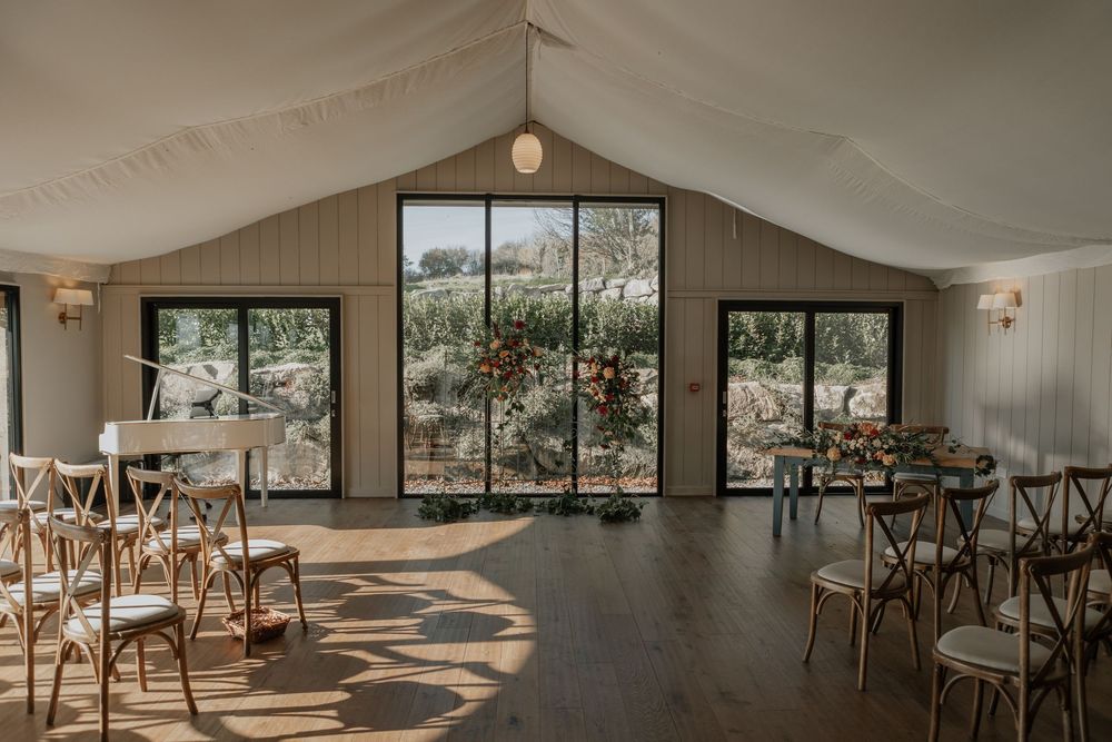 Bright airy wedding ceremony room with cross-back chairs, floral arch, and panoramic garden views.