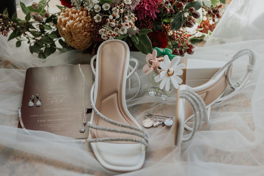 Bridal accessories flat lay featuring strappy heels, drop earrings, floral hair comb and wedding invitation.