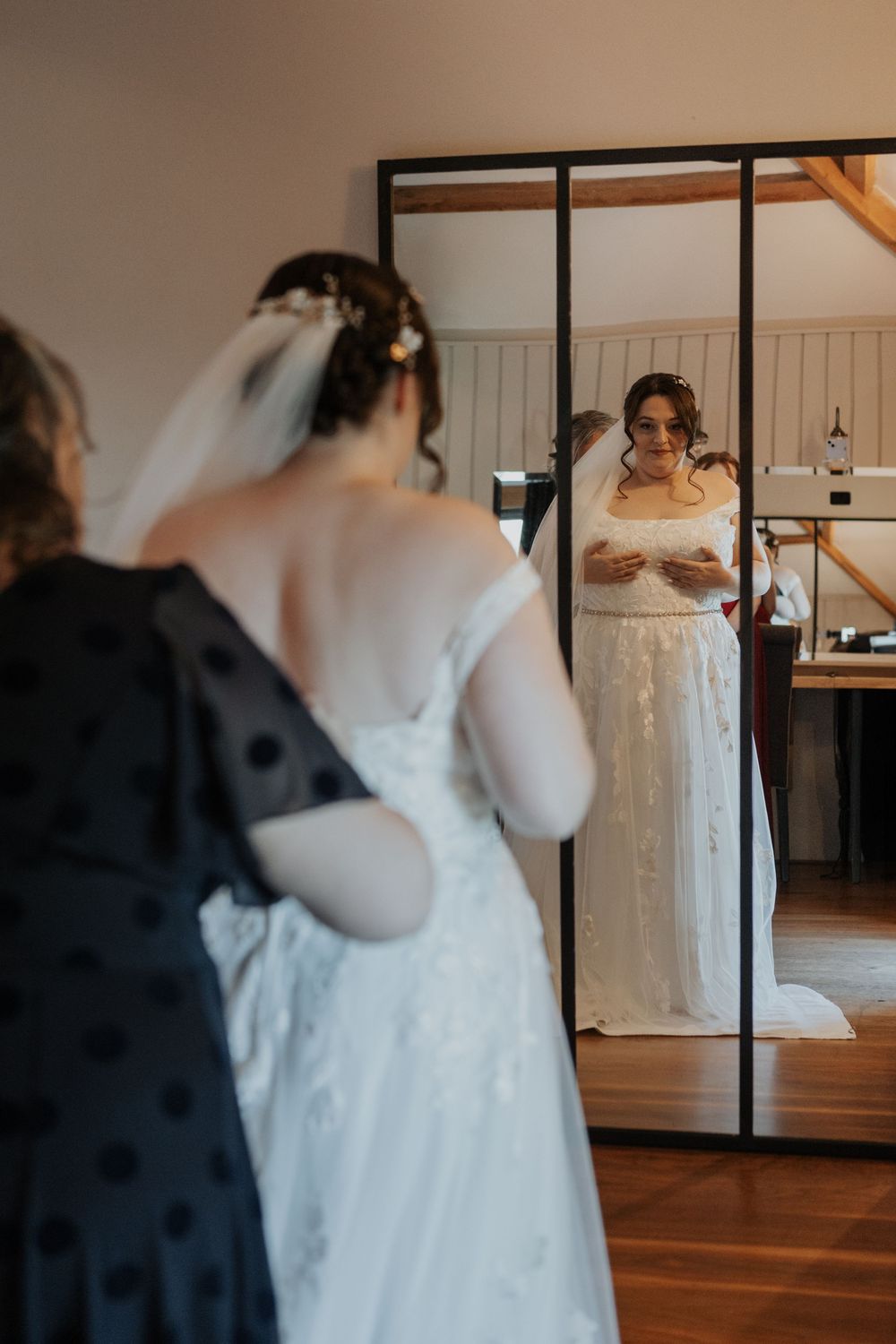 Bride in white lace wedding gown viewing her reflection in a full-length mirror during bridal prep.