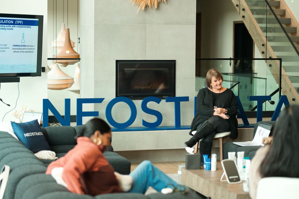 People relaxing in a modern office lounge area with blue Neostrata lettering on the wall and a fireplace.
