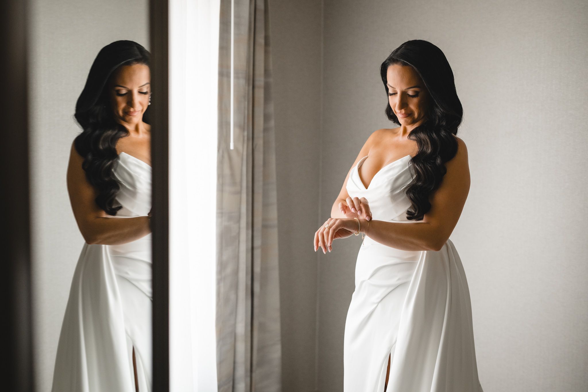 Bride in white dress poses by window in elegant black and white portrait.