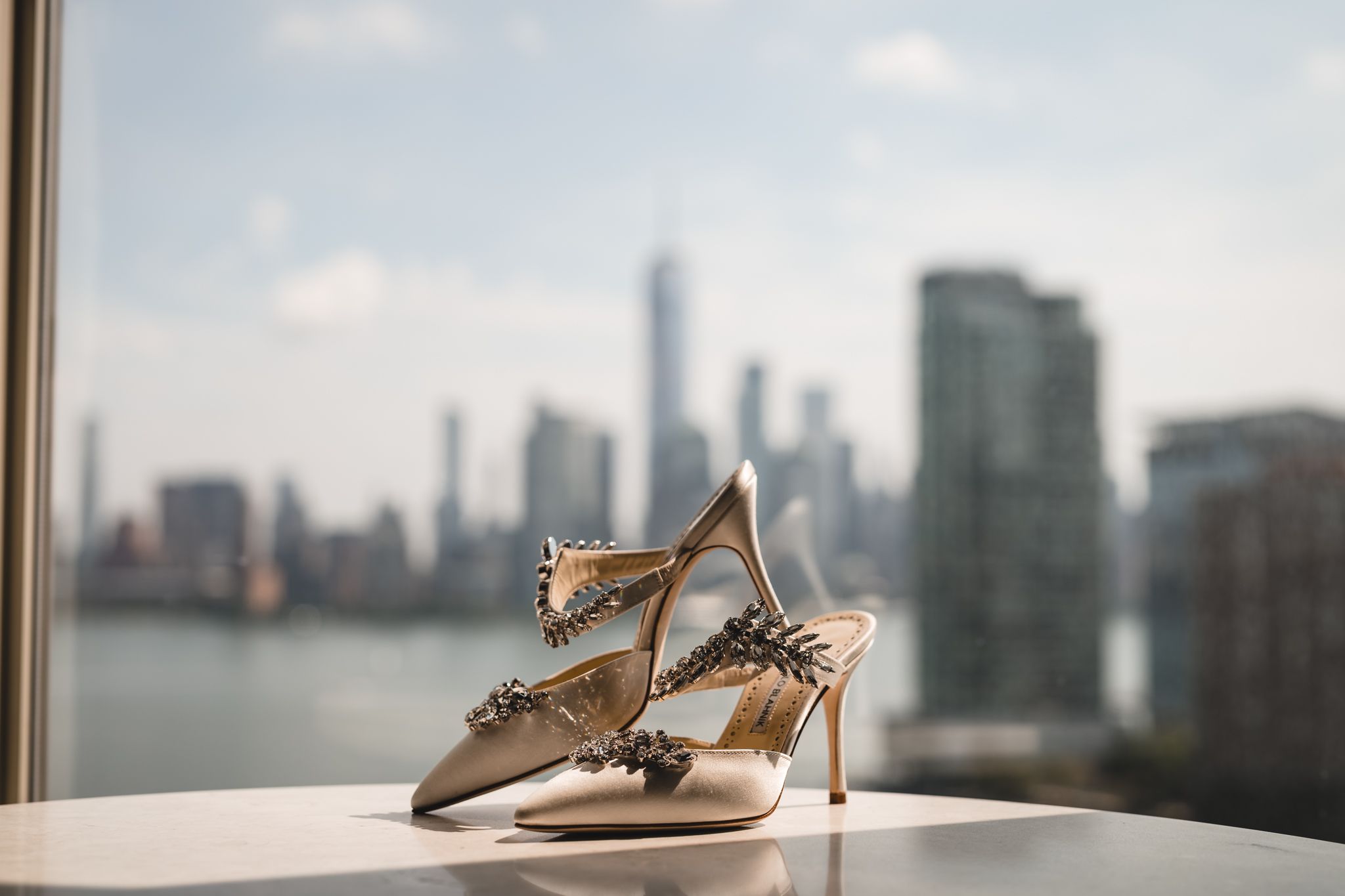 Beige high heels displayed against a city skyline backdrop through large windows.