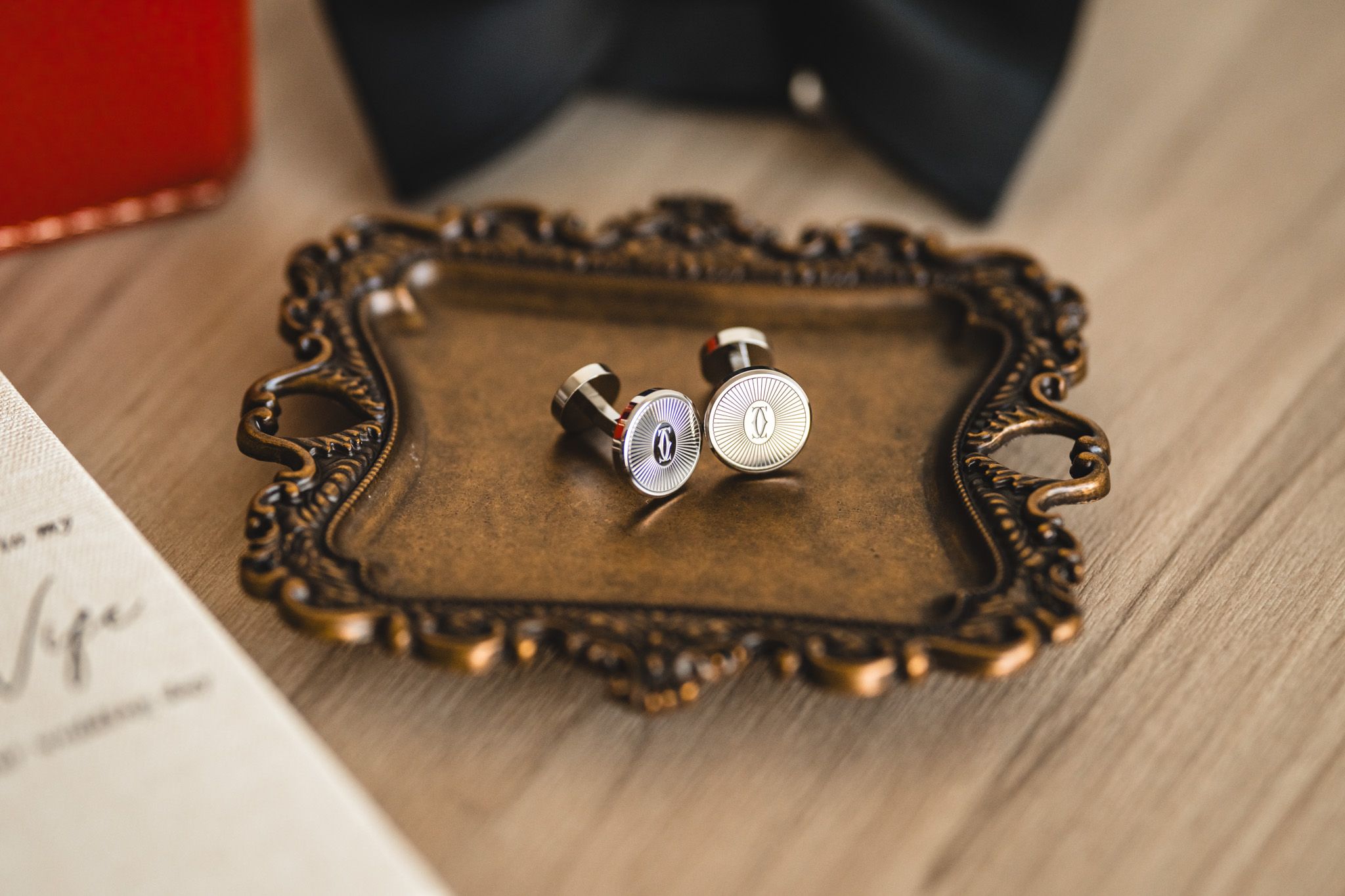 Wedding cufflinks displayed on ornate vintage tray with decorative details.