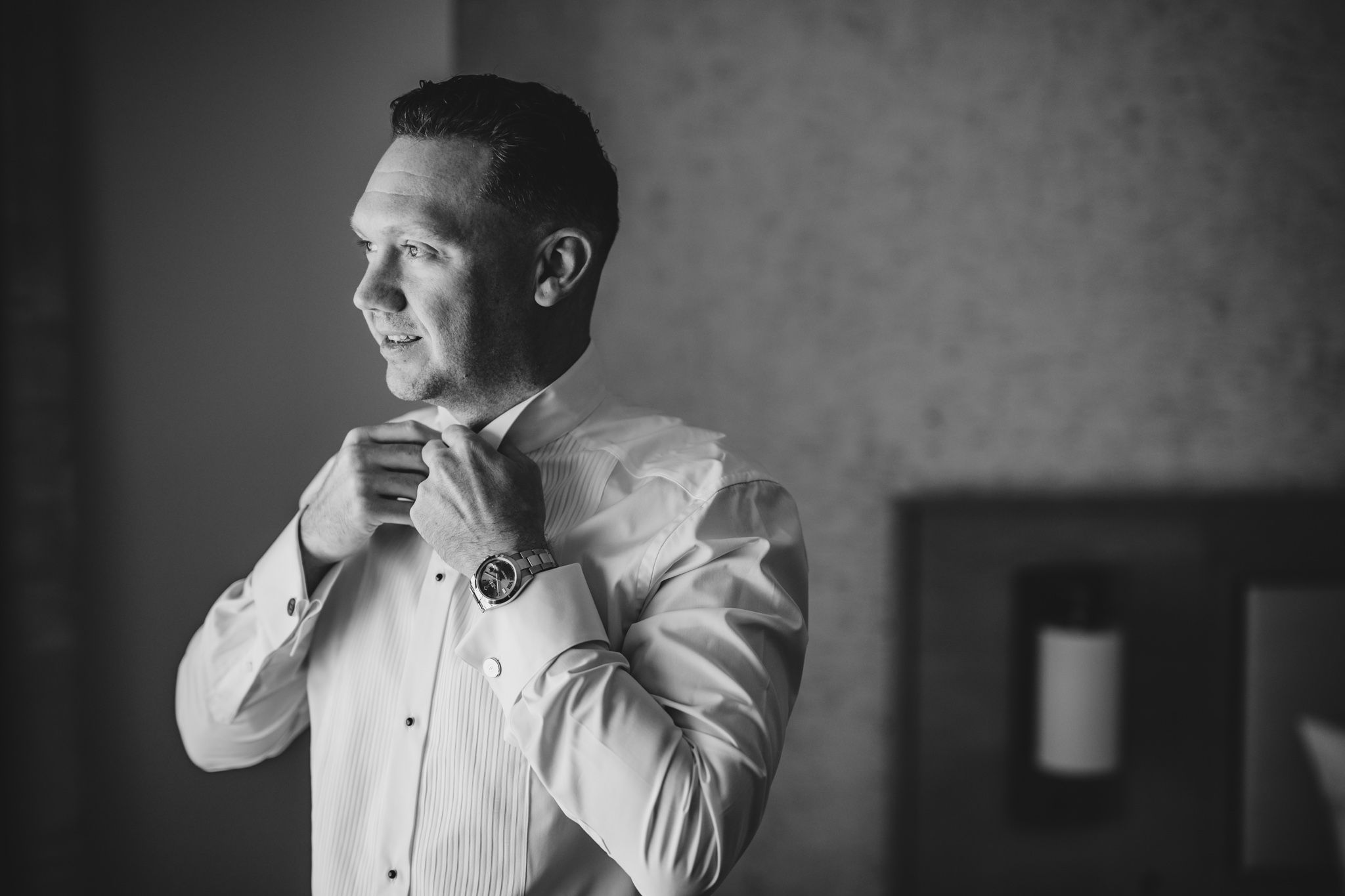 Groom adjusts bowtie while getting ready in classic black and white portrait.