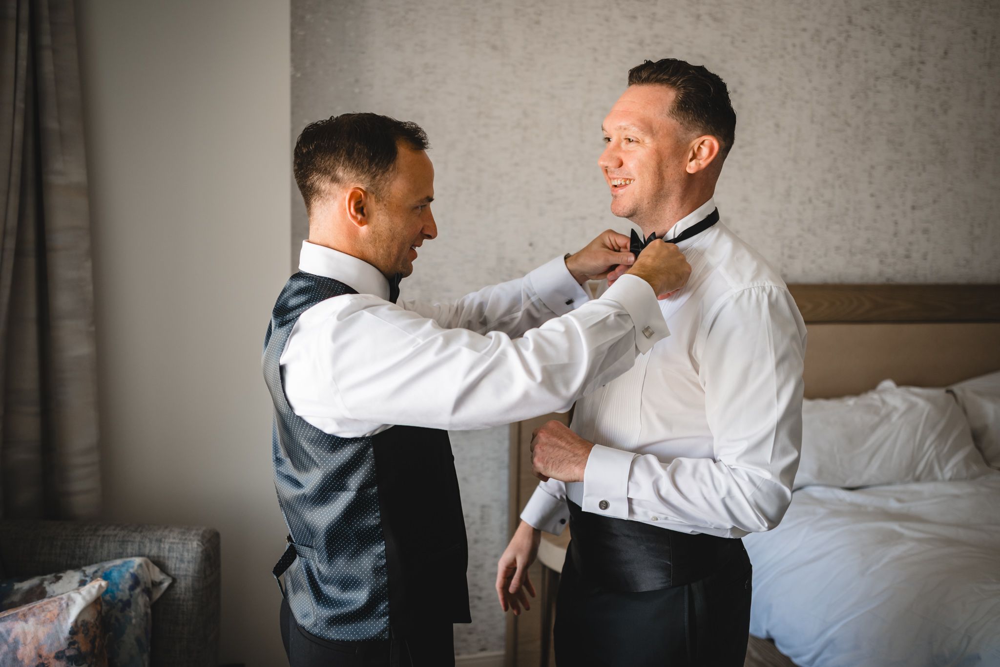 Two people in formal attire help each other prepare in a hotel room.