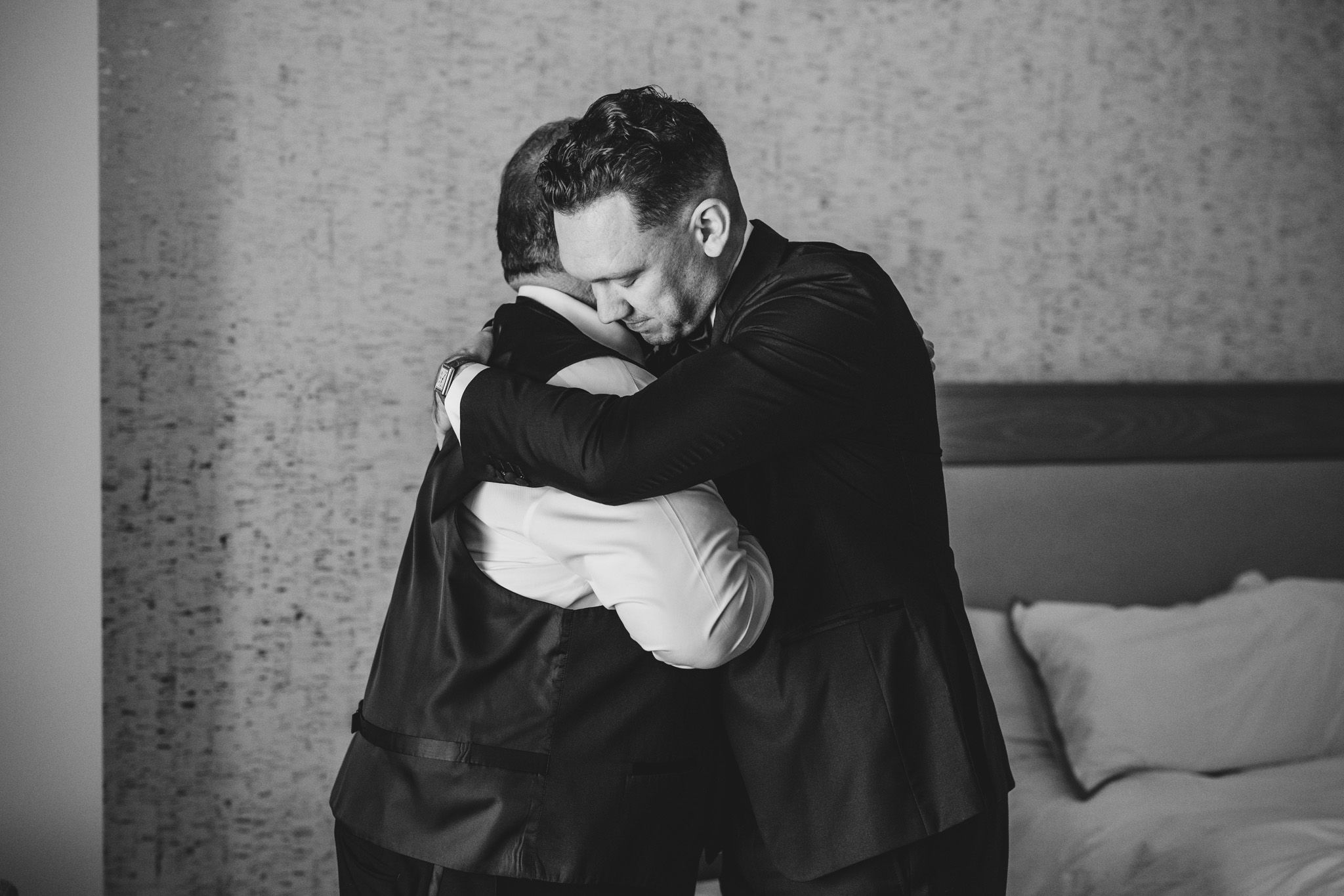 Two people in formal attire embrace while preparing for a special occasion.