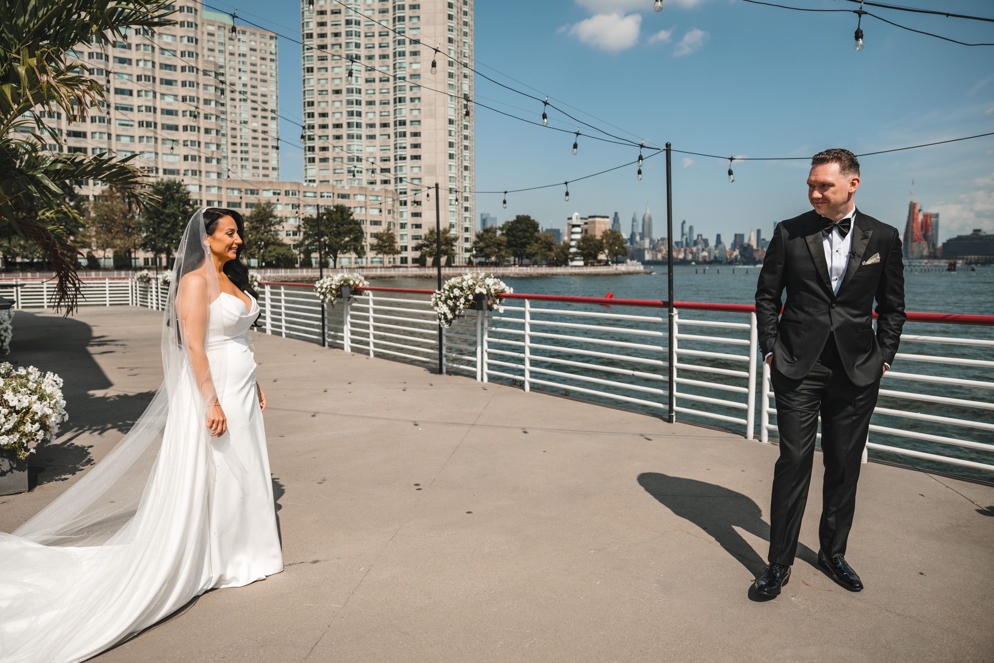Wedding couple poses on a waterfront deck with city buildings in the background.
