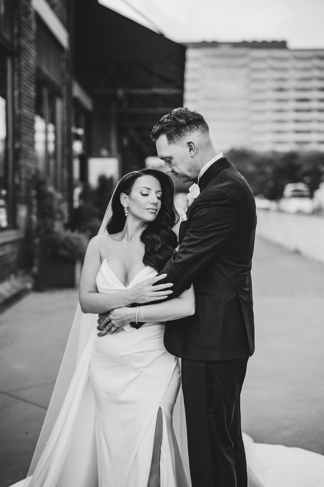 Elegant couple shares tender moments in their wedding attire against an urban backdrop.