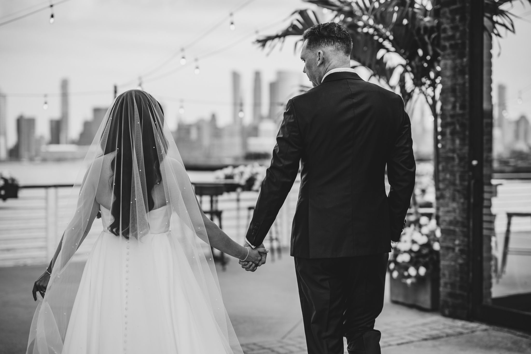 Wedding couple poses against city skyline with palm trees and string lights creating a romantic atmosphere.