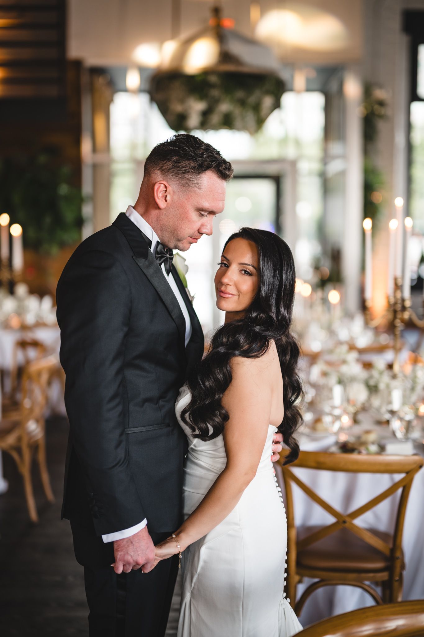 Romantic moment between newlyweds in an elegant reception venue with wooden chairs and tables.