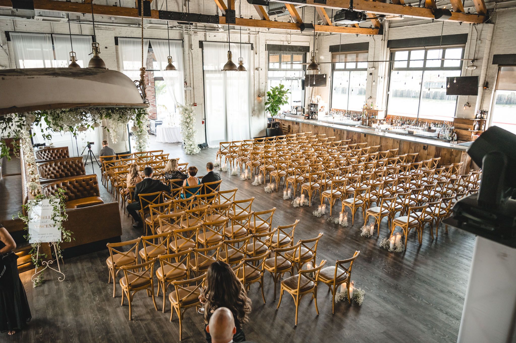 Industrial wedding ceremony space with rows of wooden chairs and large windows.