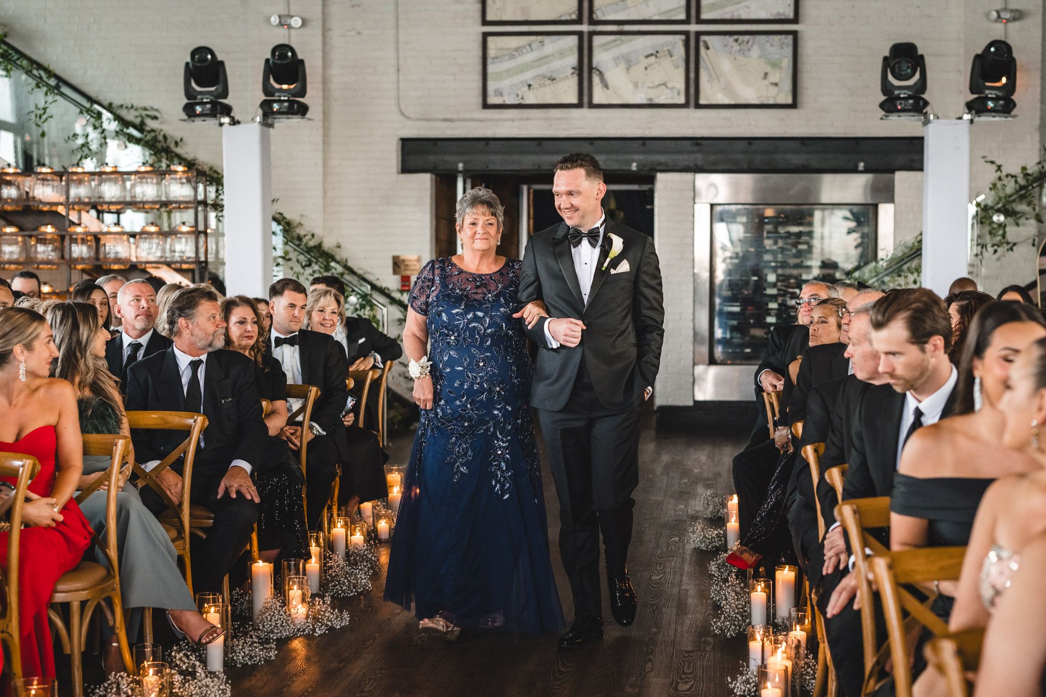 Wedding ceremony processional in modern industrial venue with guests seated in wooden chairs.