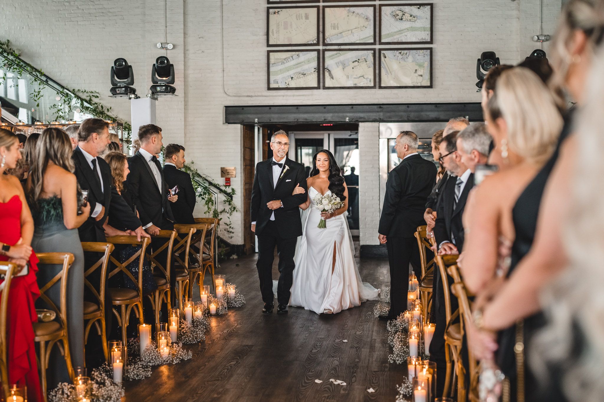 Wedding ceremony aisle lined with wooden chairs in industrial-style venue with white walls.