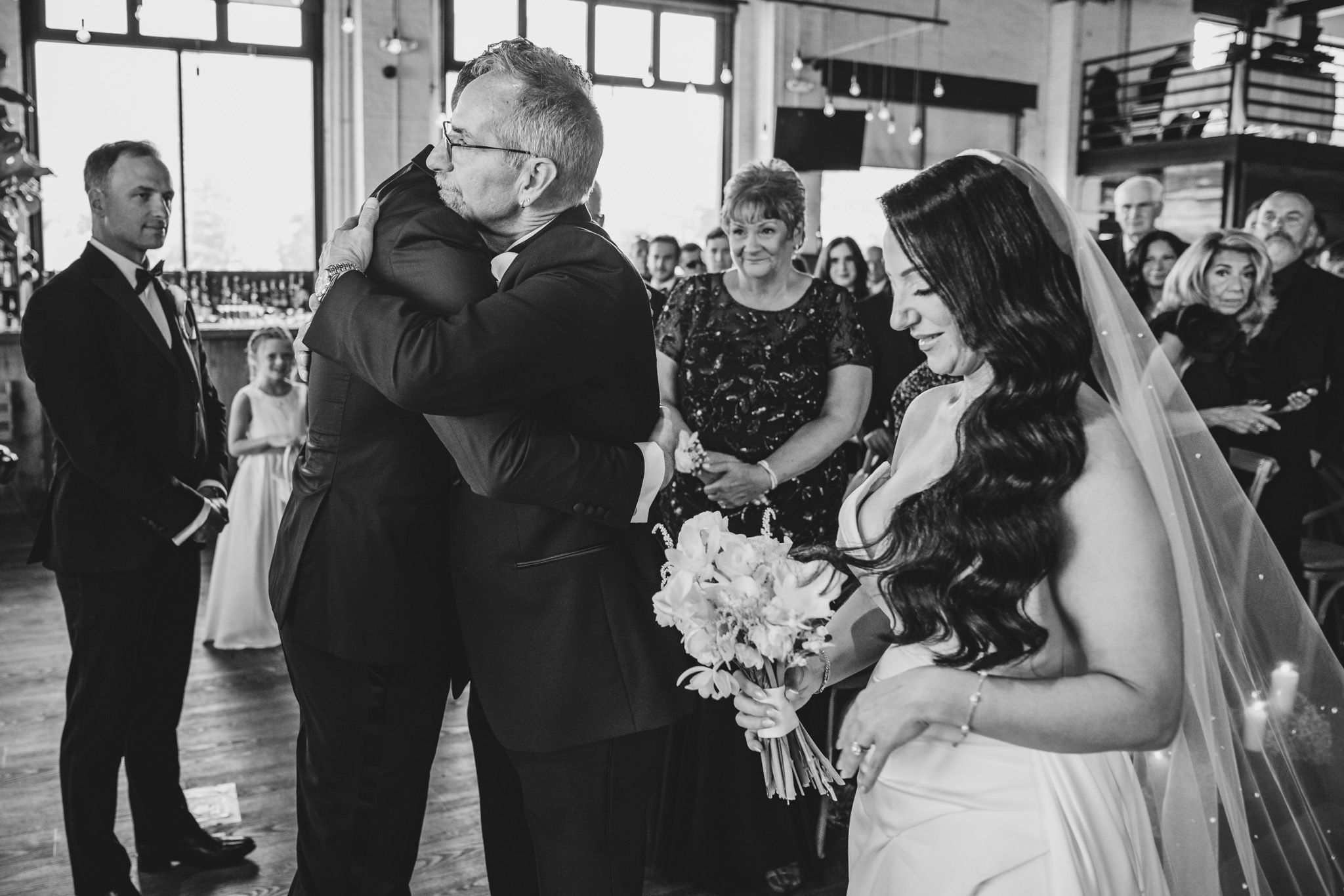 Black and white photo of wedding ceremony guests in industrial venue with natural lighting.