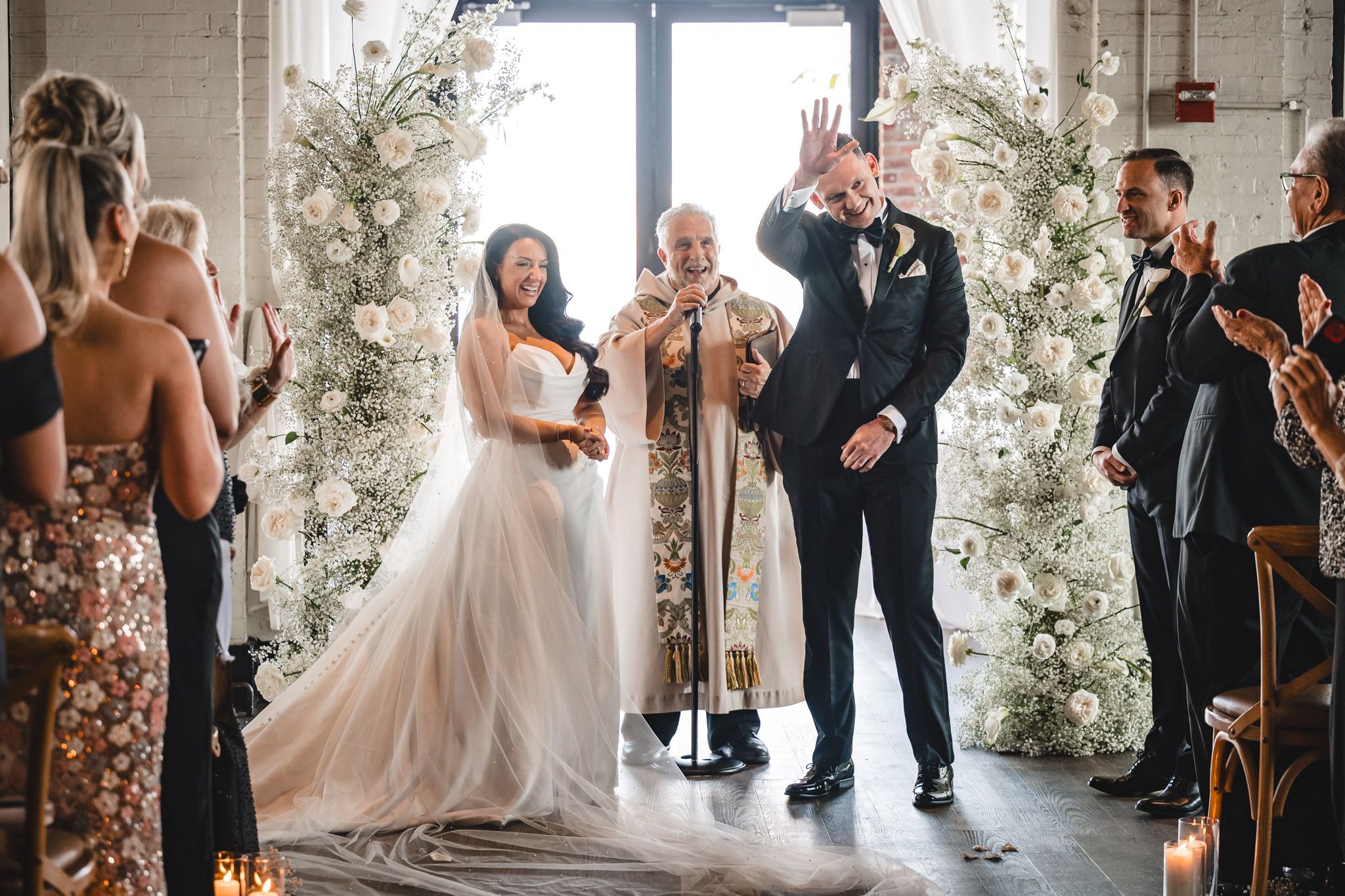 Wedding ceremony space decorated with white floral arrangements and wooden cross-back chairs.