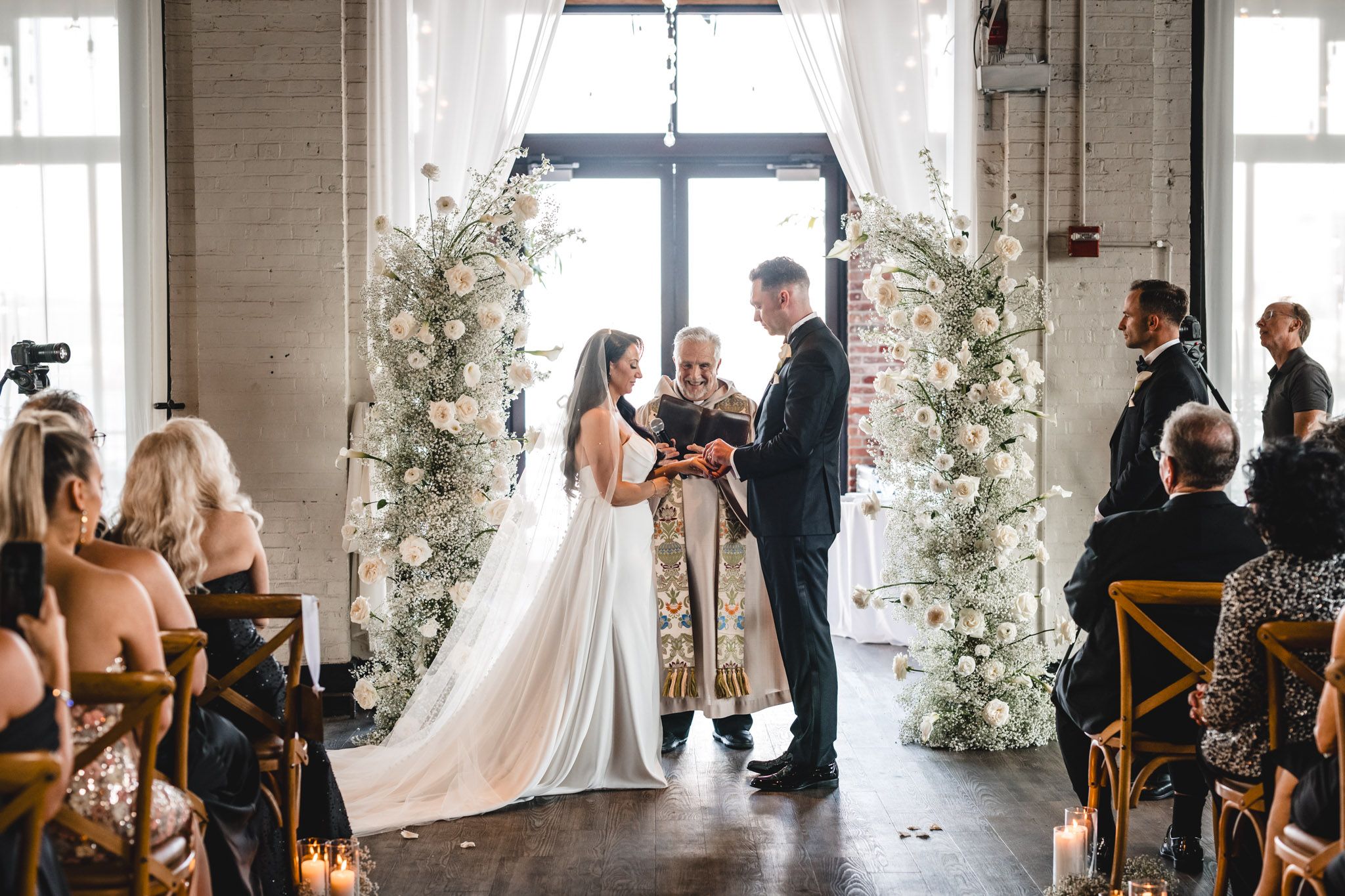 Wedding ceremony in an industrial chic venue with floral arch and natural light streaming through windows.