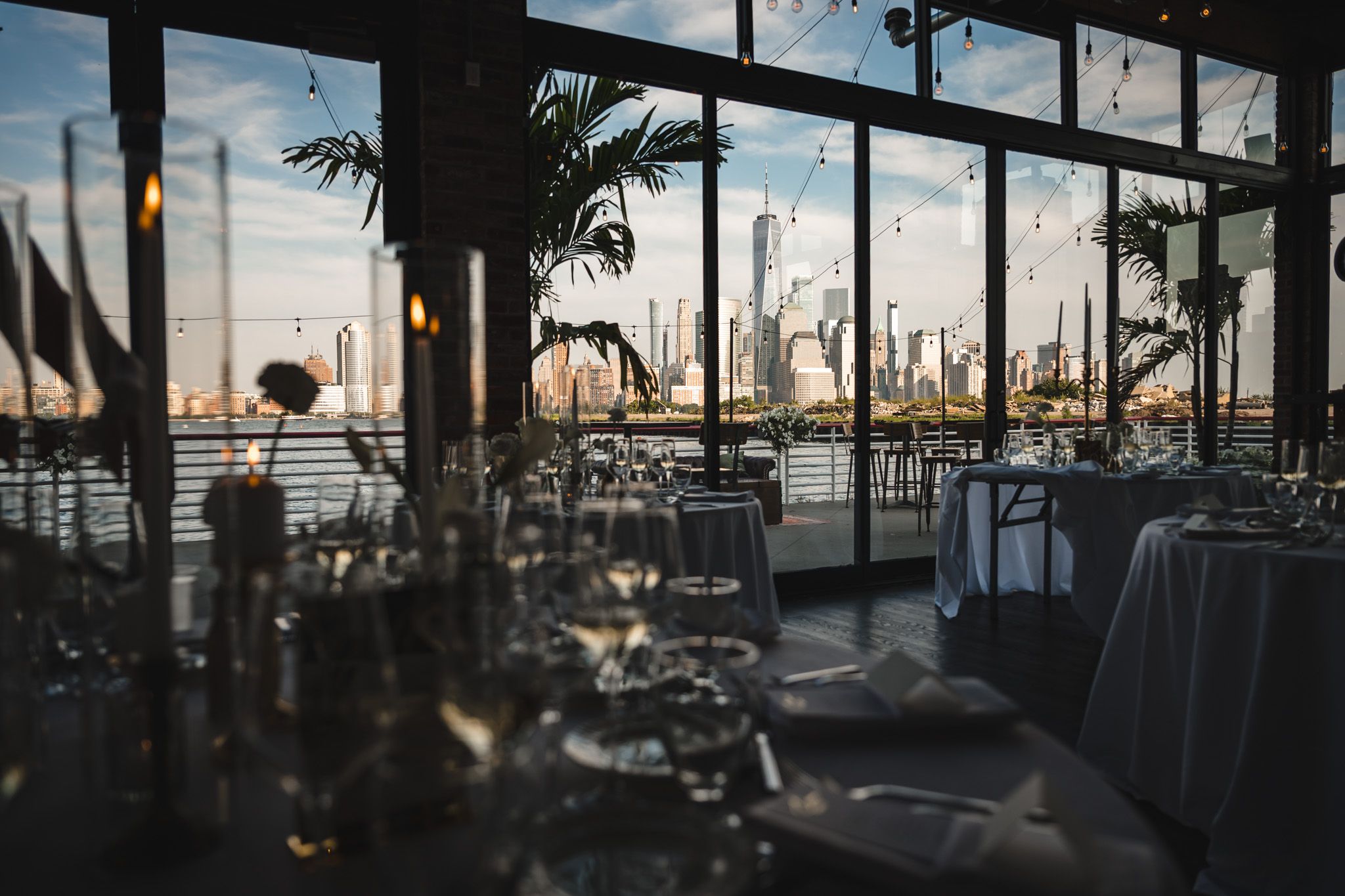 Wedding reception venue with city skyline view through large windows at sunset.