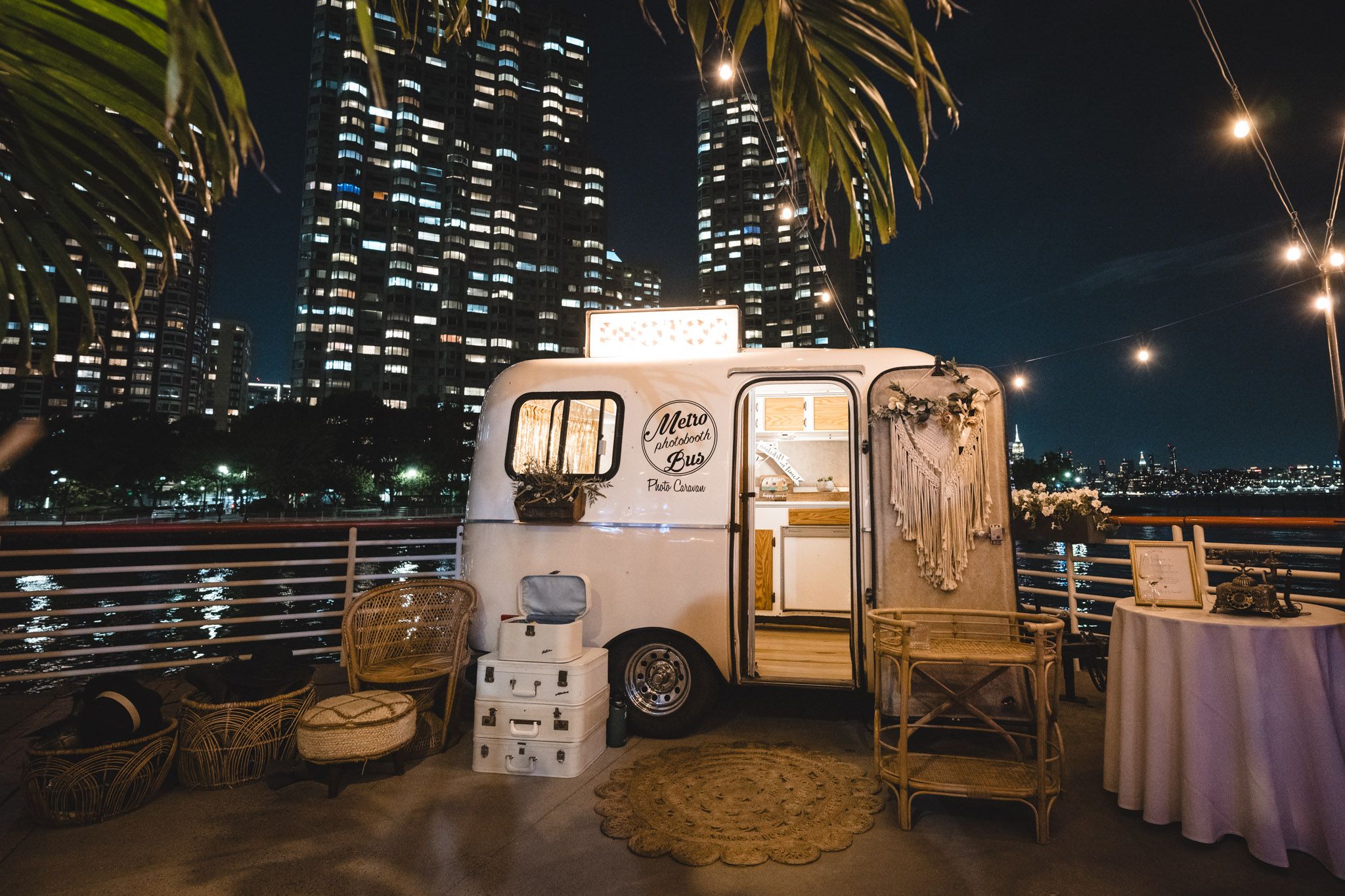 Nighttime cityscape with food trucks and tables set up against illuminated high-rise buildings.