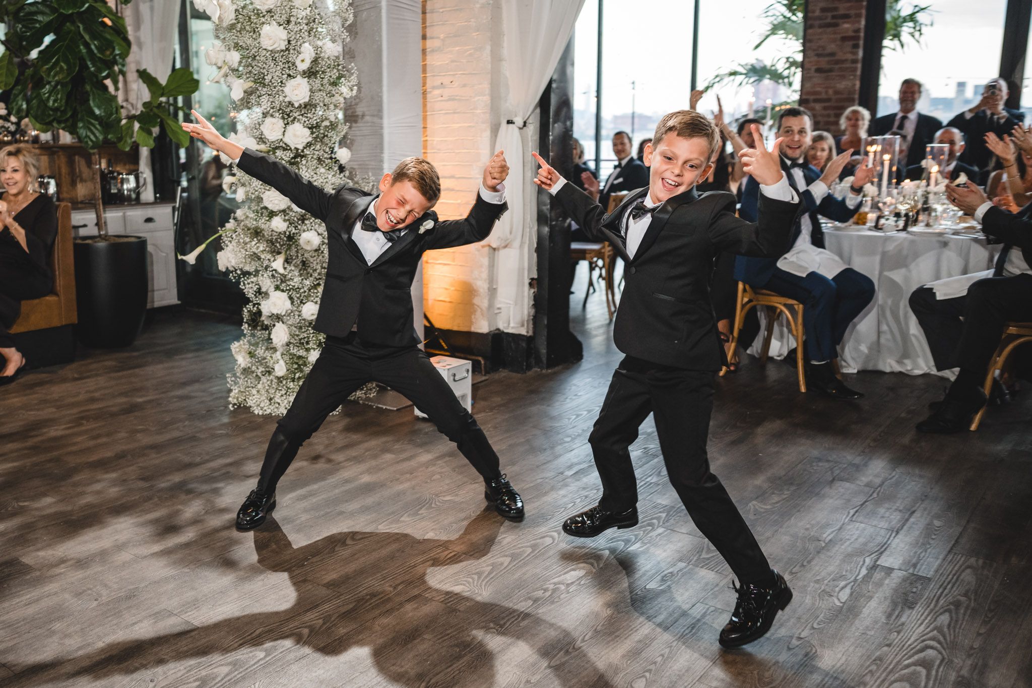 Wedding celebration with dancing guests on a wooden floor in an indoor venue.