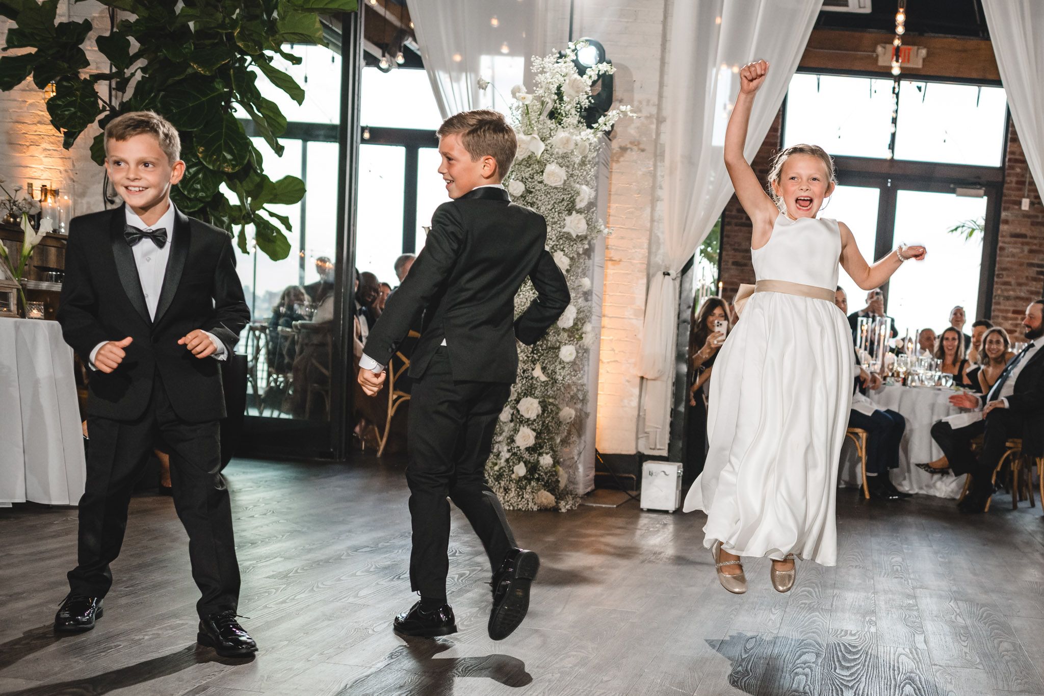 Wedding party dancing and celebrating on hardwood floors in an industrial-style venue.