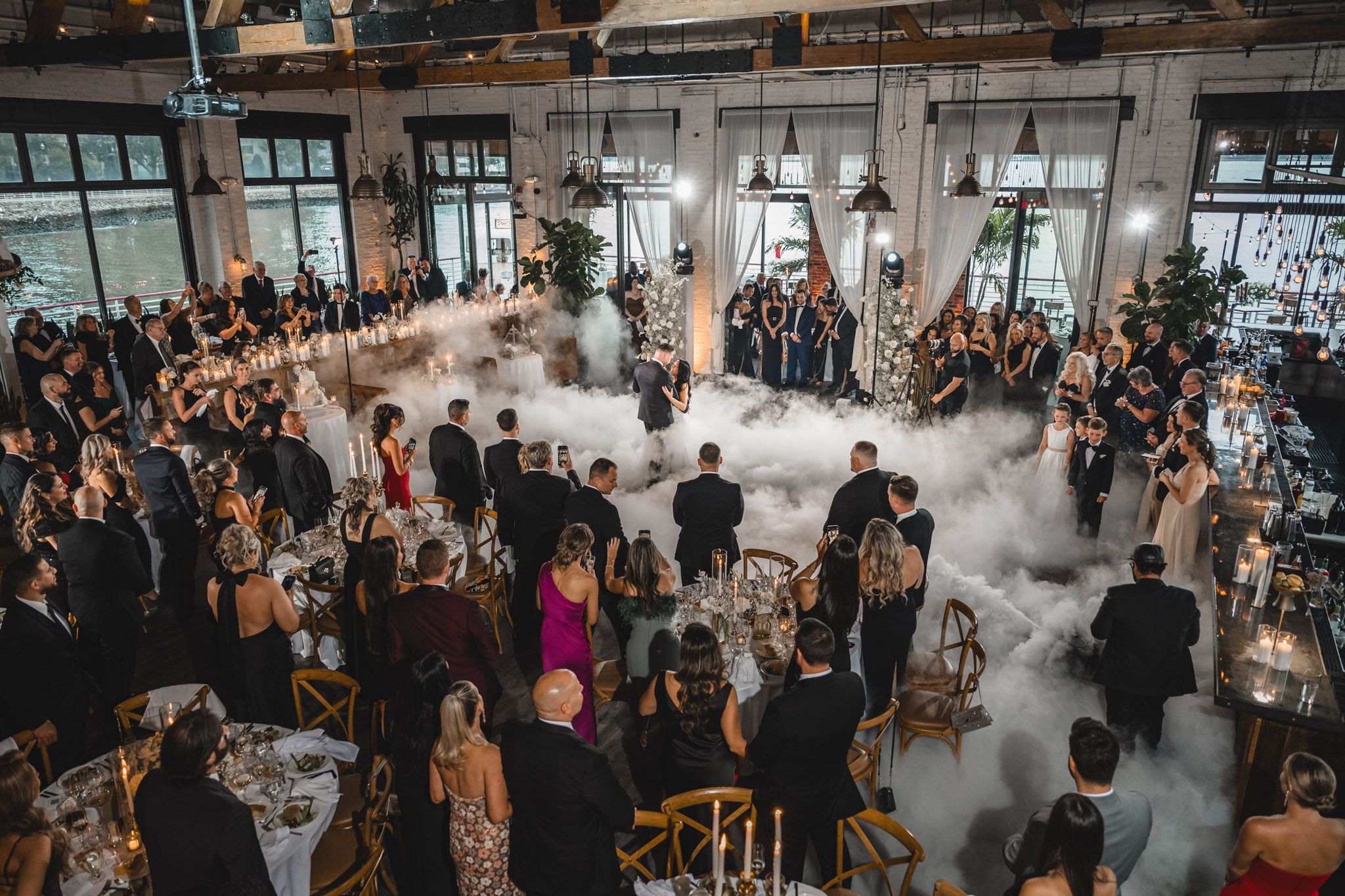 Wide view of a wedding reception venue filled with guests and atmospheric lighting.