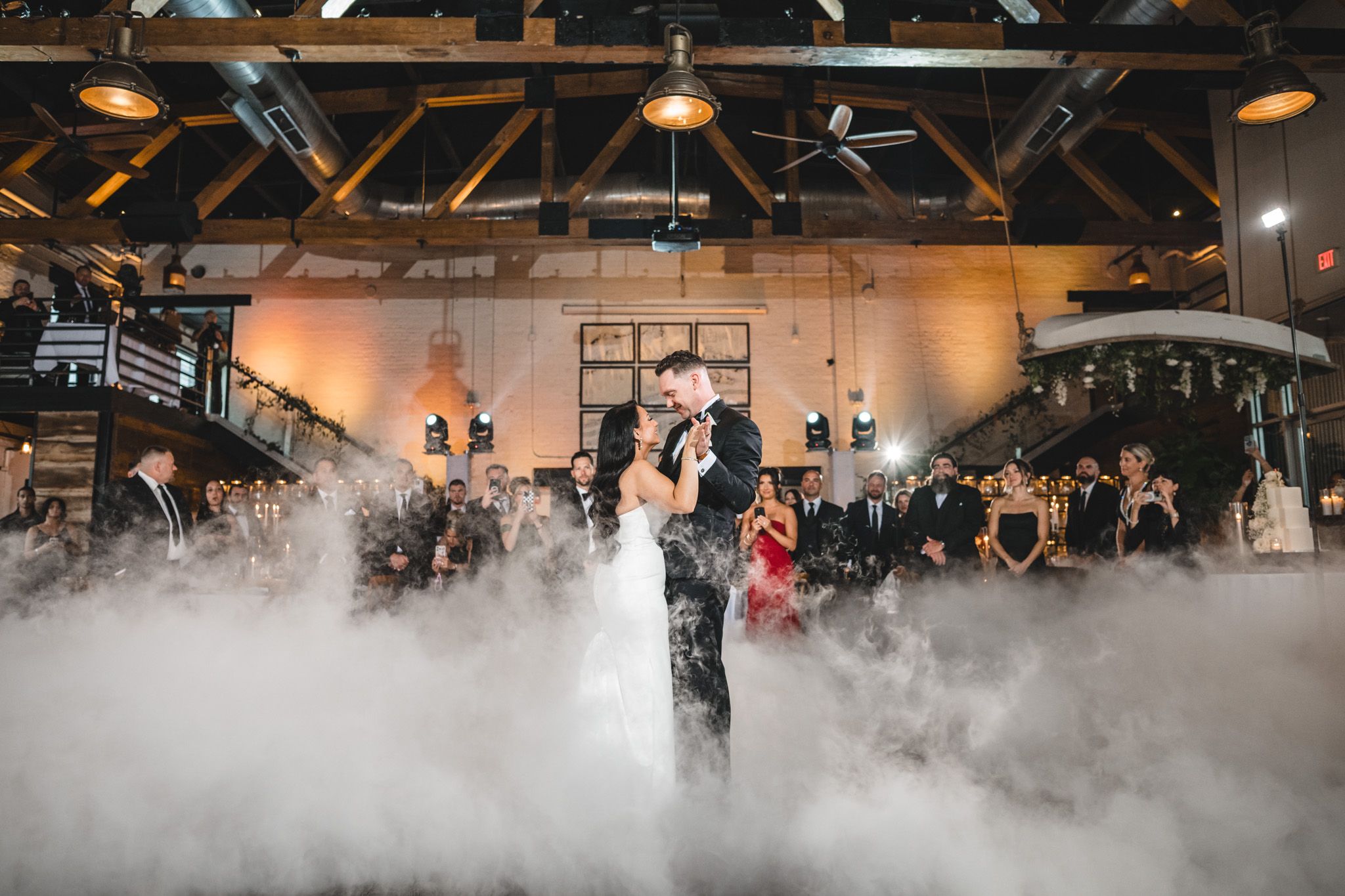 Couple dancing in a romantic first dance surrounded by atmospheric fog effects at an indoor wedding reception.