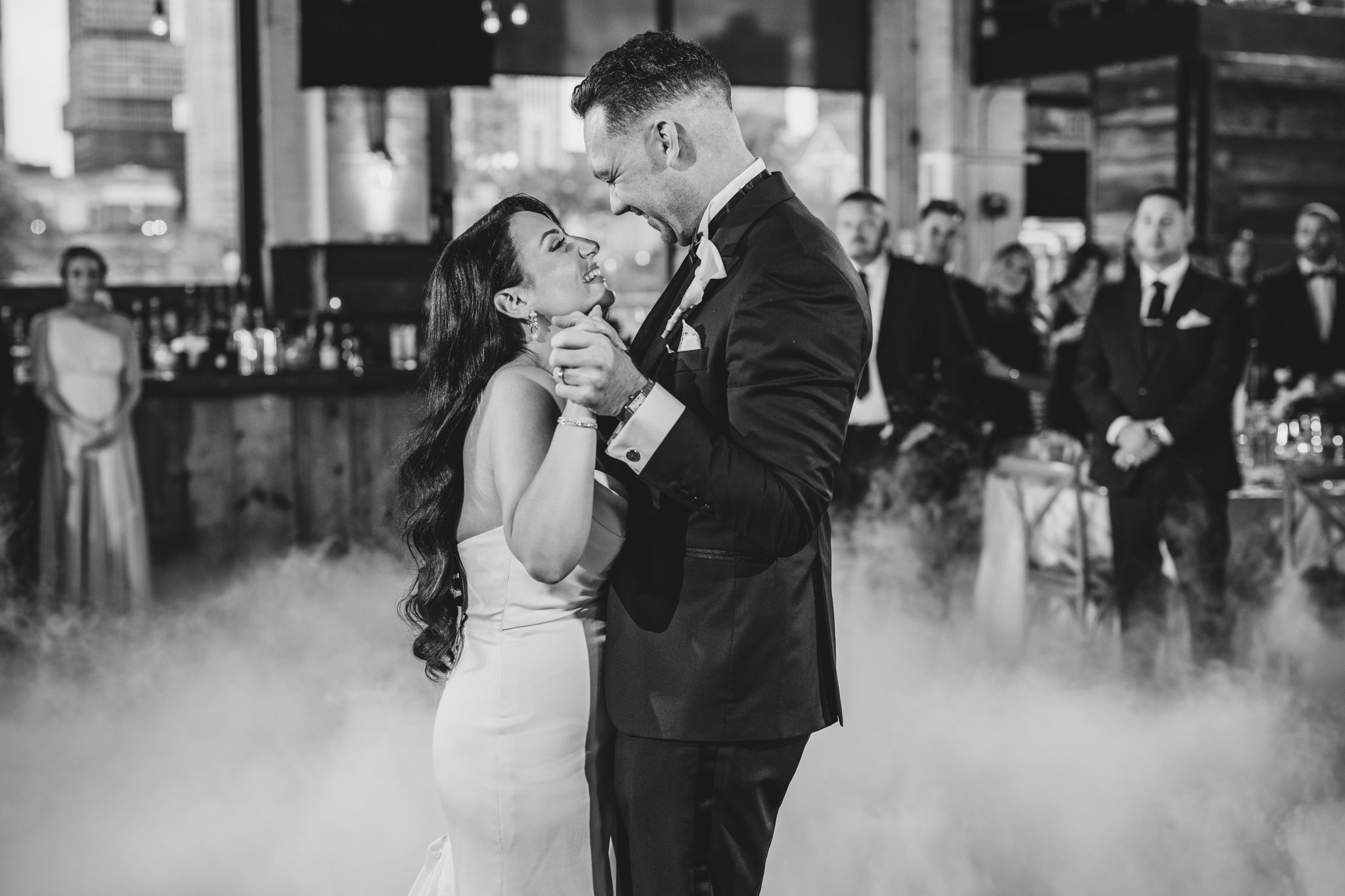 Wedding couple shares an intimate dance moment on a misty dance floor with dramatic lighting effects.