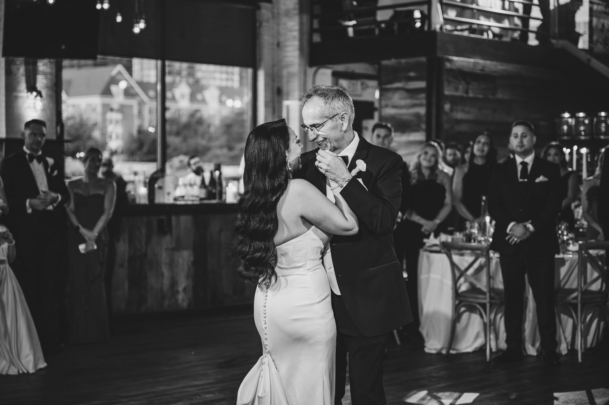 Newlyweds perform their first dance in a beautifully lit indoor venue with guests watching.