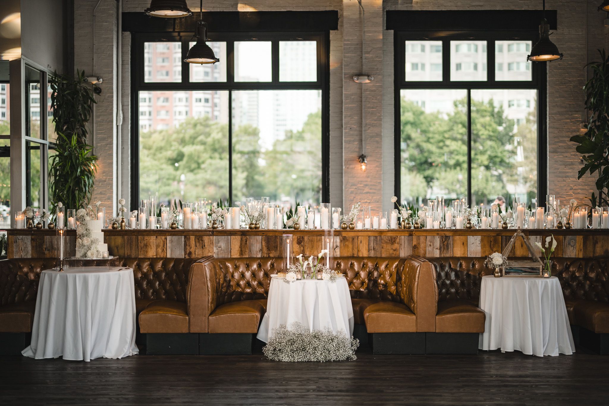 Elegant wedding reception setup with white linens and wooden chairs against industrial windows.