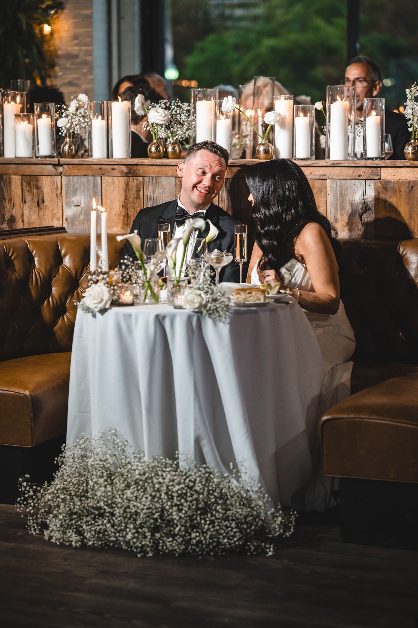 Wedding reception table decorated with white linens and baby's breath flowers against rustic decor.