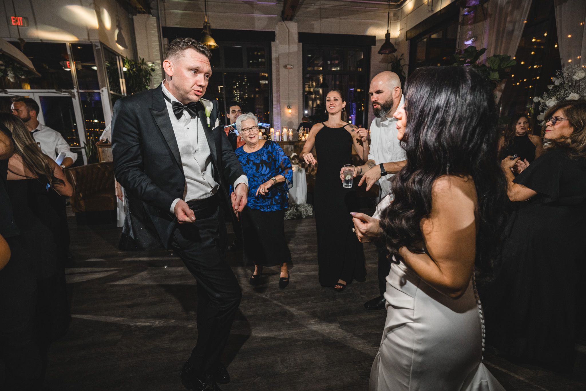 Wedding party dancing and mingling in a modern industrial venue with exposed ceiling.