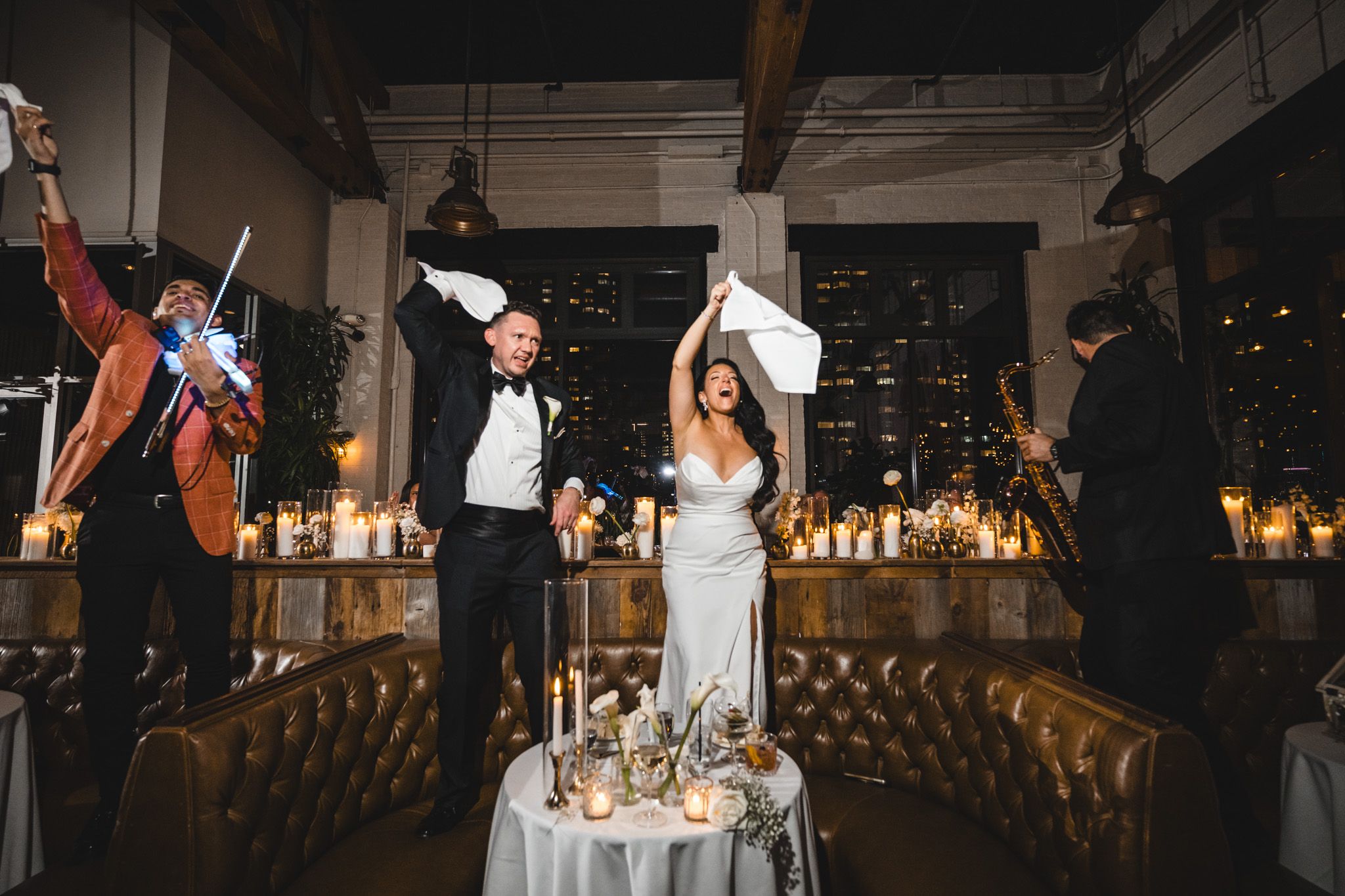 Wedding reception venue features exposed industrial ceiling and elegant lighting over dance floor.