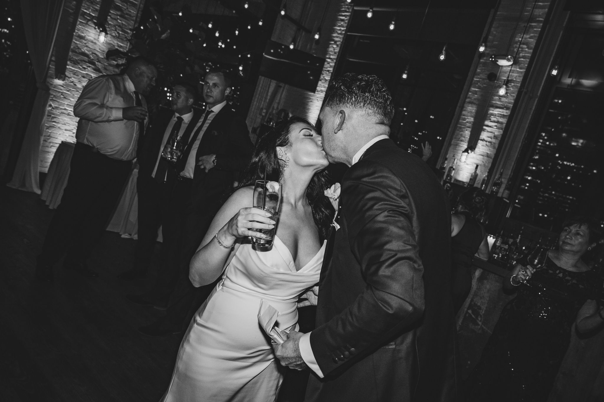 Couple dancing together at a dimly lit wedding reception with string lights overhead.