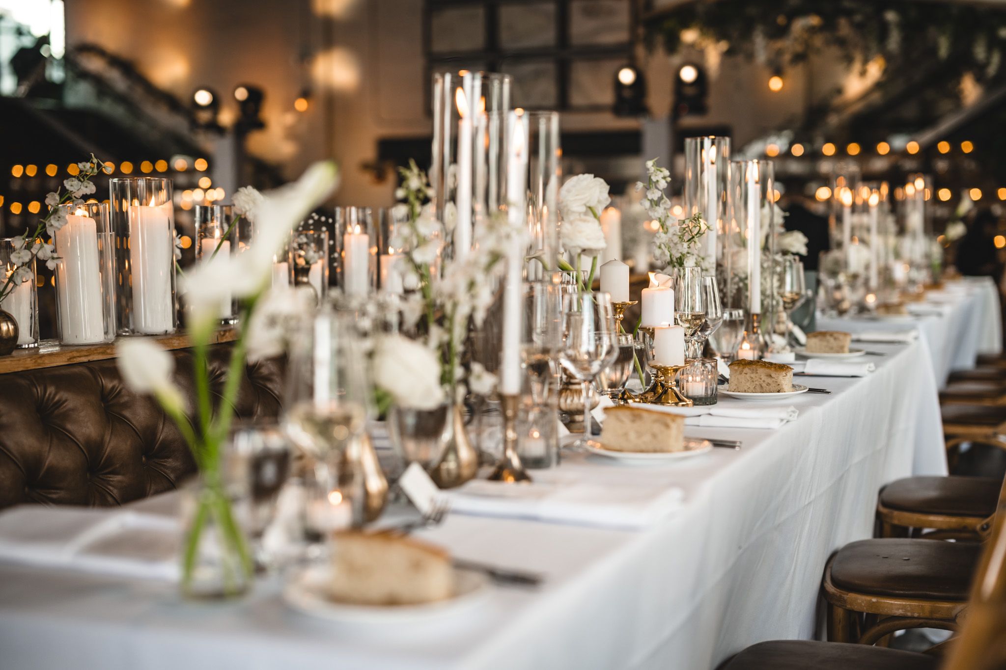 Elegant wedding reception tables set with glassware, white linens and ambient lighting.