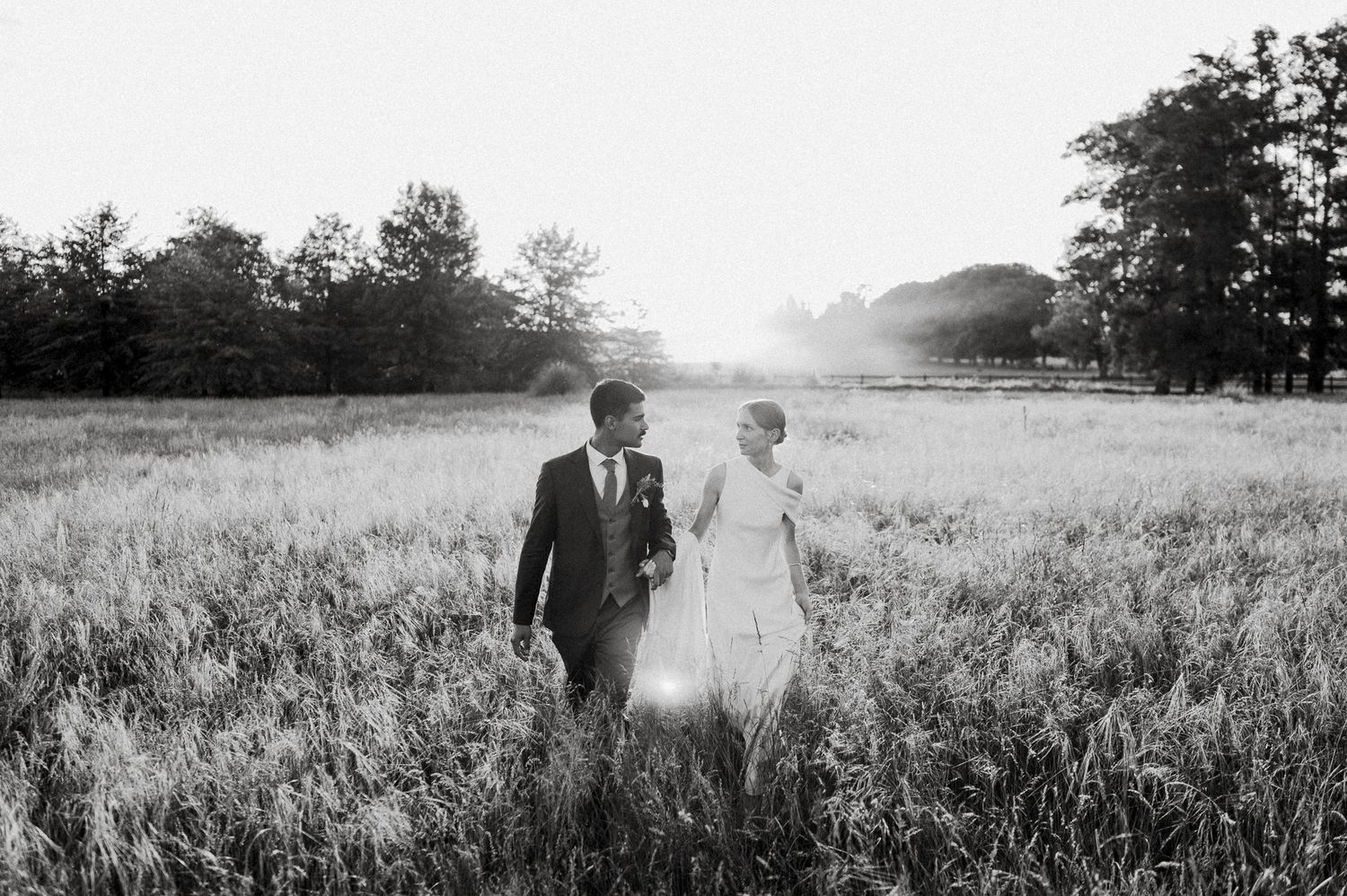 Romantic black and white photo of newlyweds walking through a misty field at sunset.