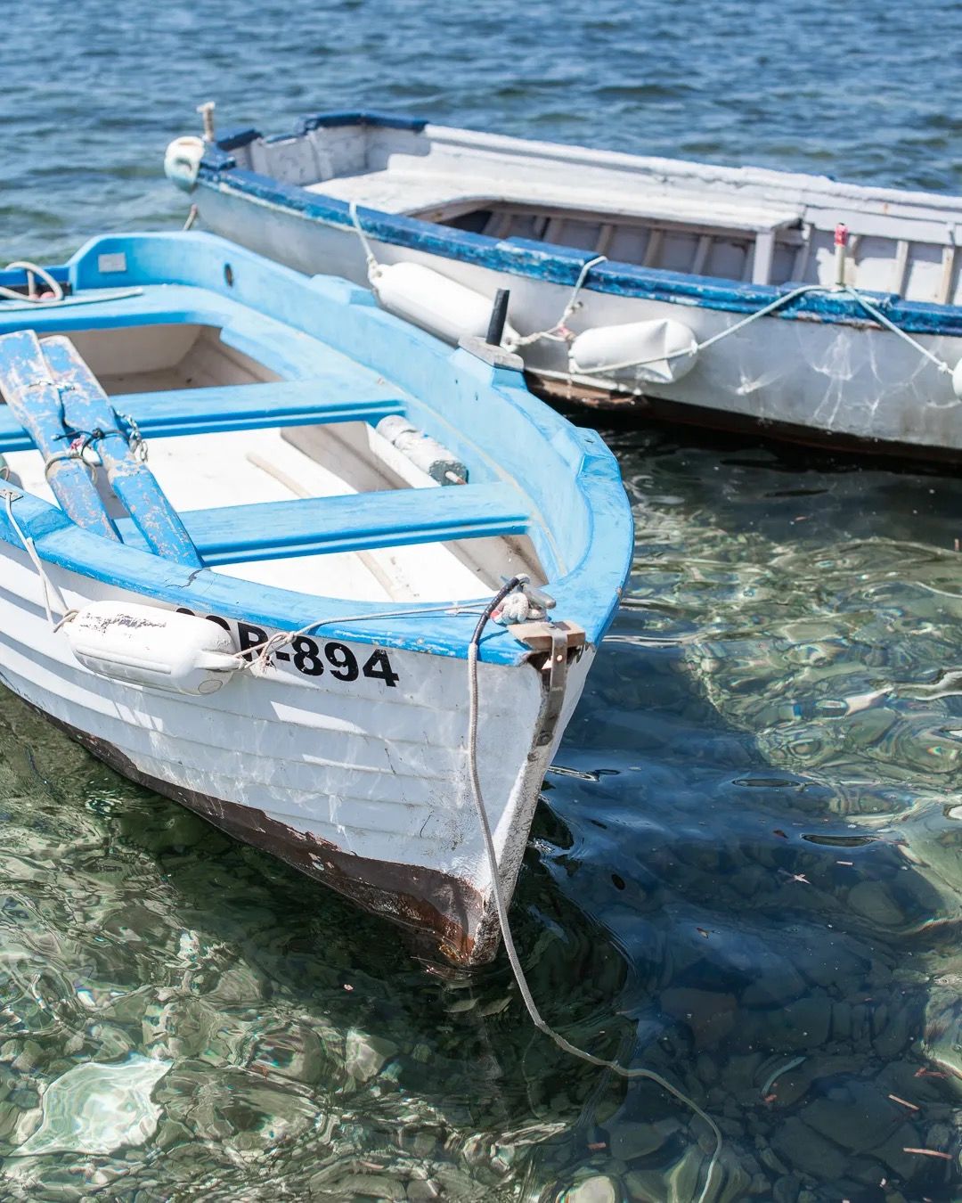 Blue wooden boats tied together and floating on crystal-clear water in a sunlit harbour.