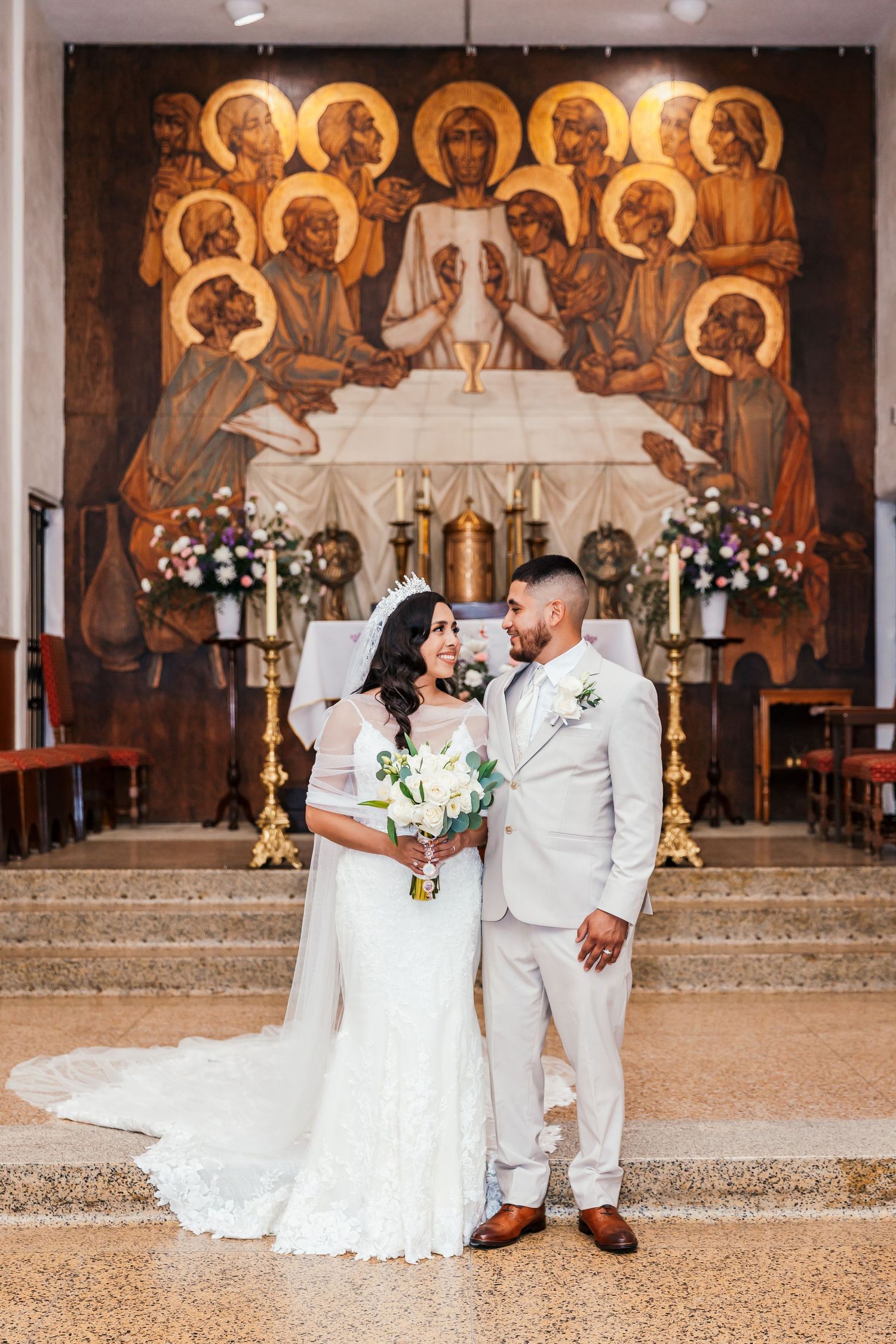 Bride and groom standing at a church altar beneath a stunning mosaic of the Last Supper.