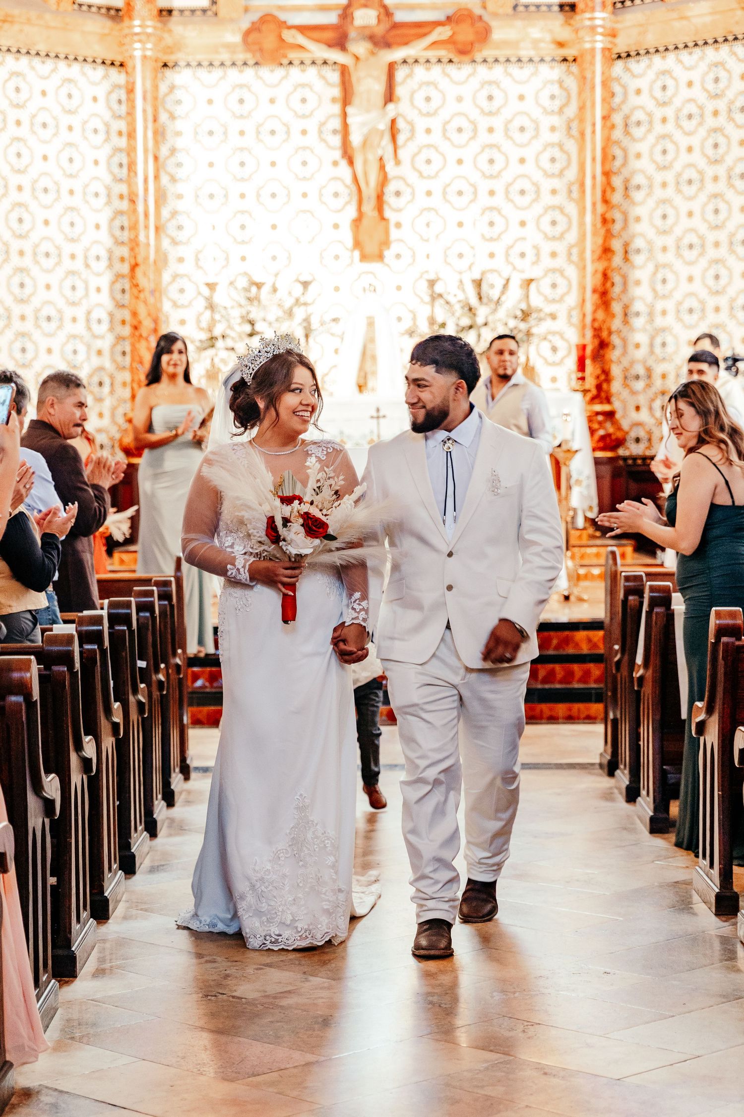 Bride and groom walking down church aisle after wedding ceremony, bride holding red and white bouquet.