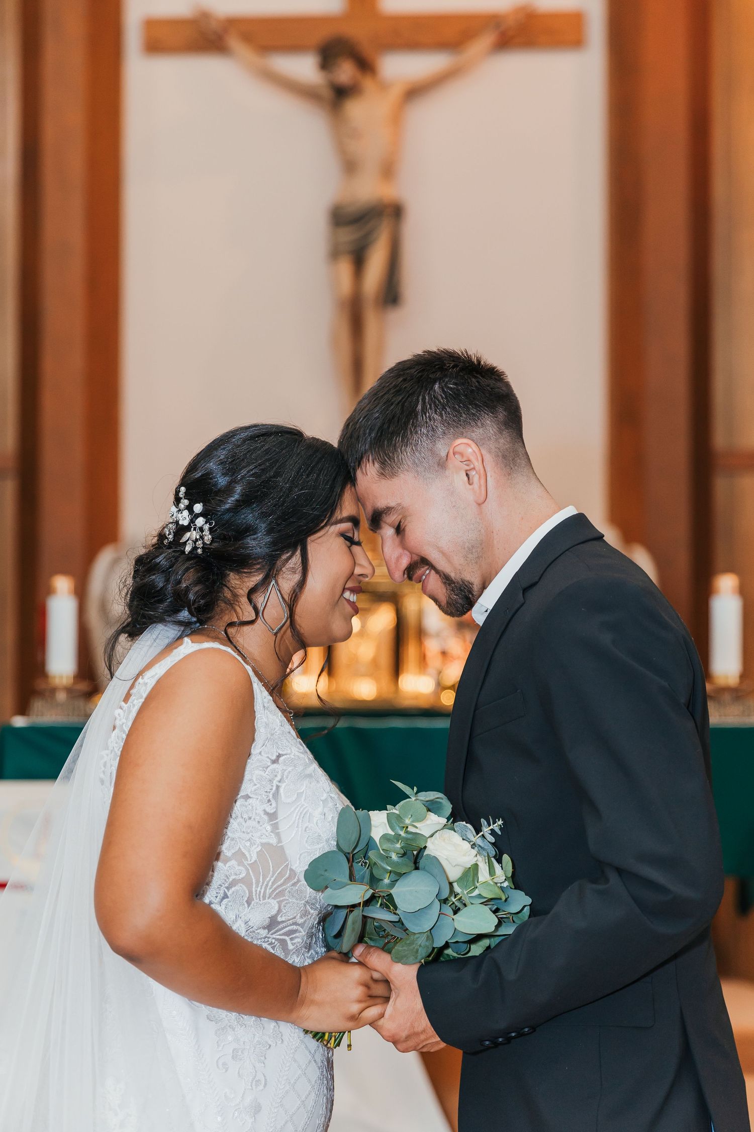 Bride and groom touching foreheads tenderly at the altar of a Catholic church.