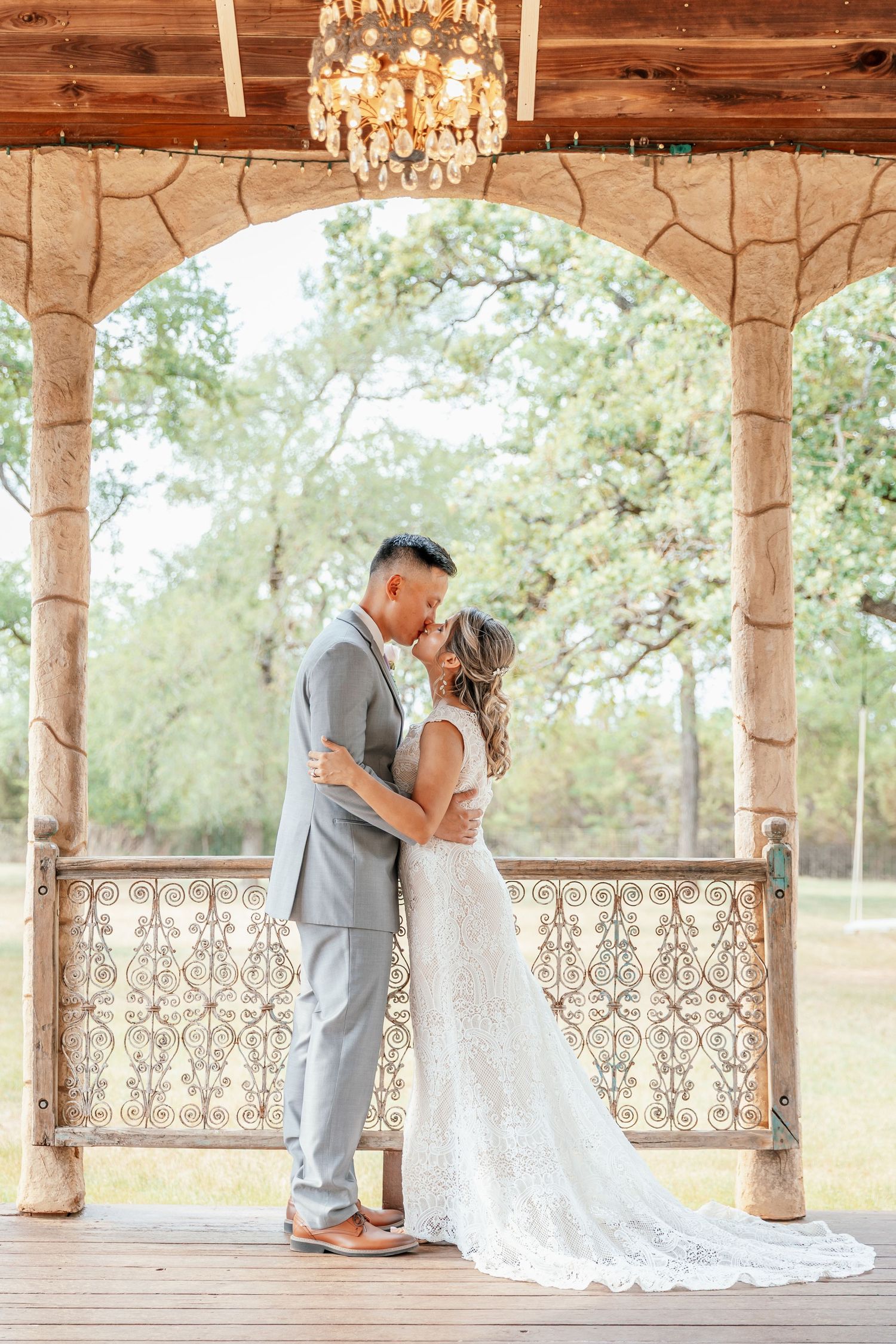 Bride and groom sharing first kiss under elegant gazebo with chandelier at wedding.