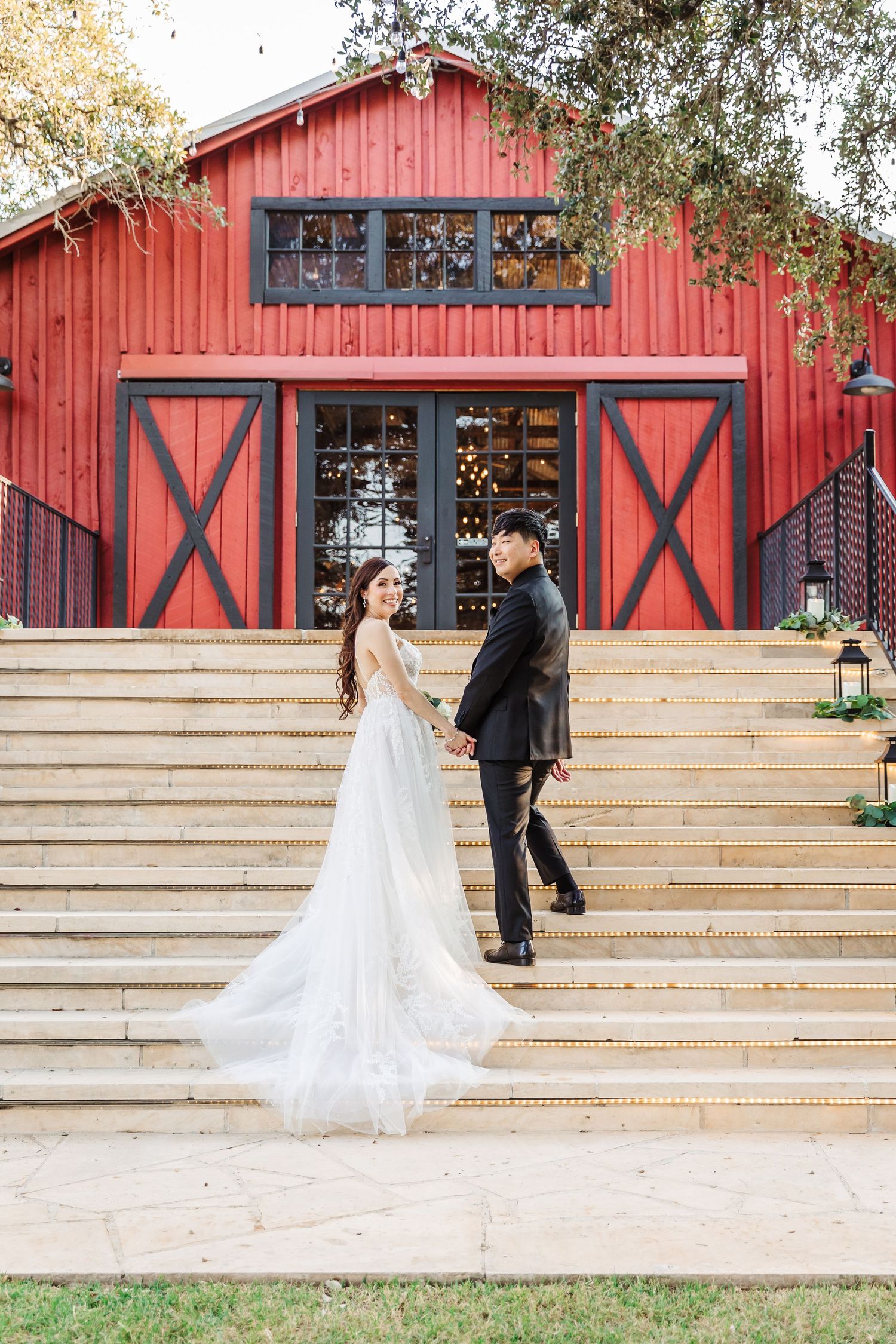 Bride and groom holding hands on steps before a rustic red barn wedding venue.