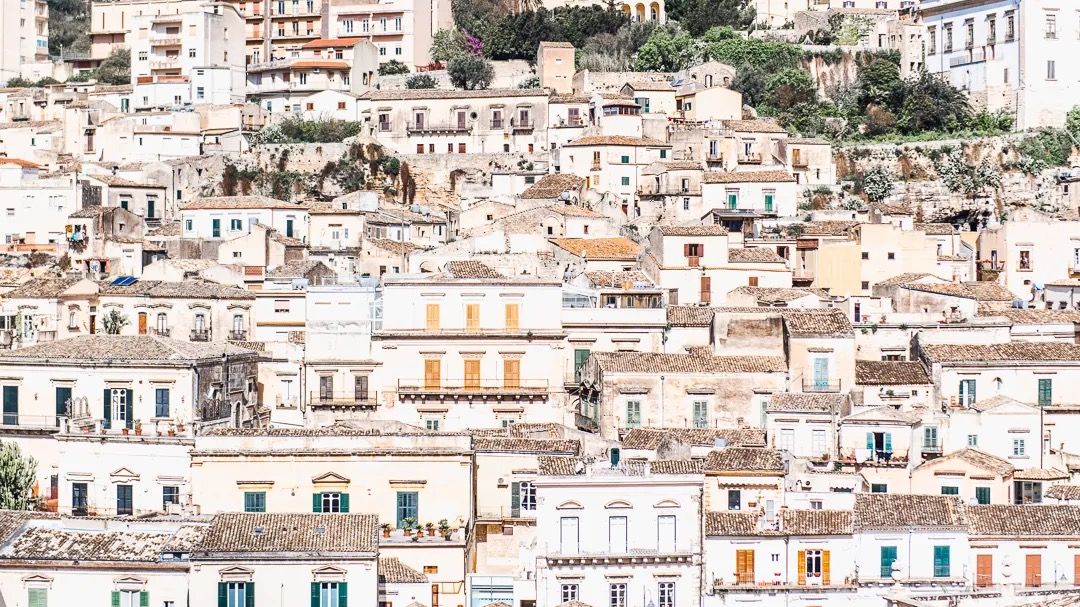 A white hillside town with tightly packed homes and terraces stretches across the landscape.