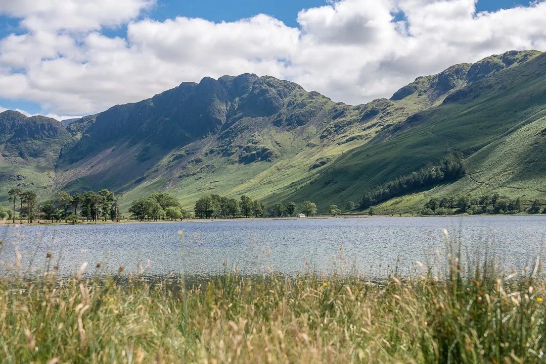 Mountain lake view with grassy shoreline and rolling green hills in sunshine.